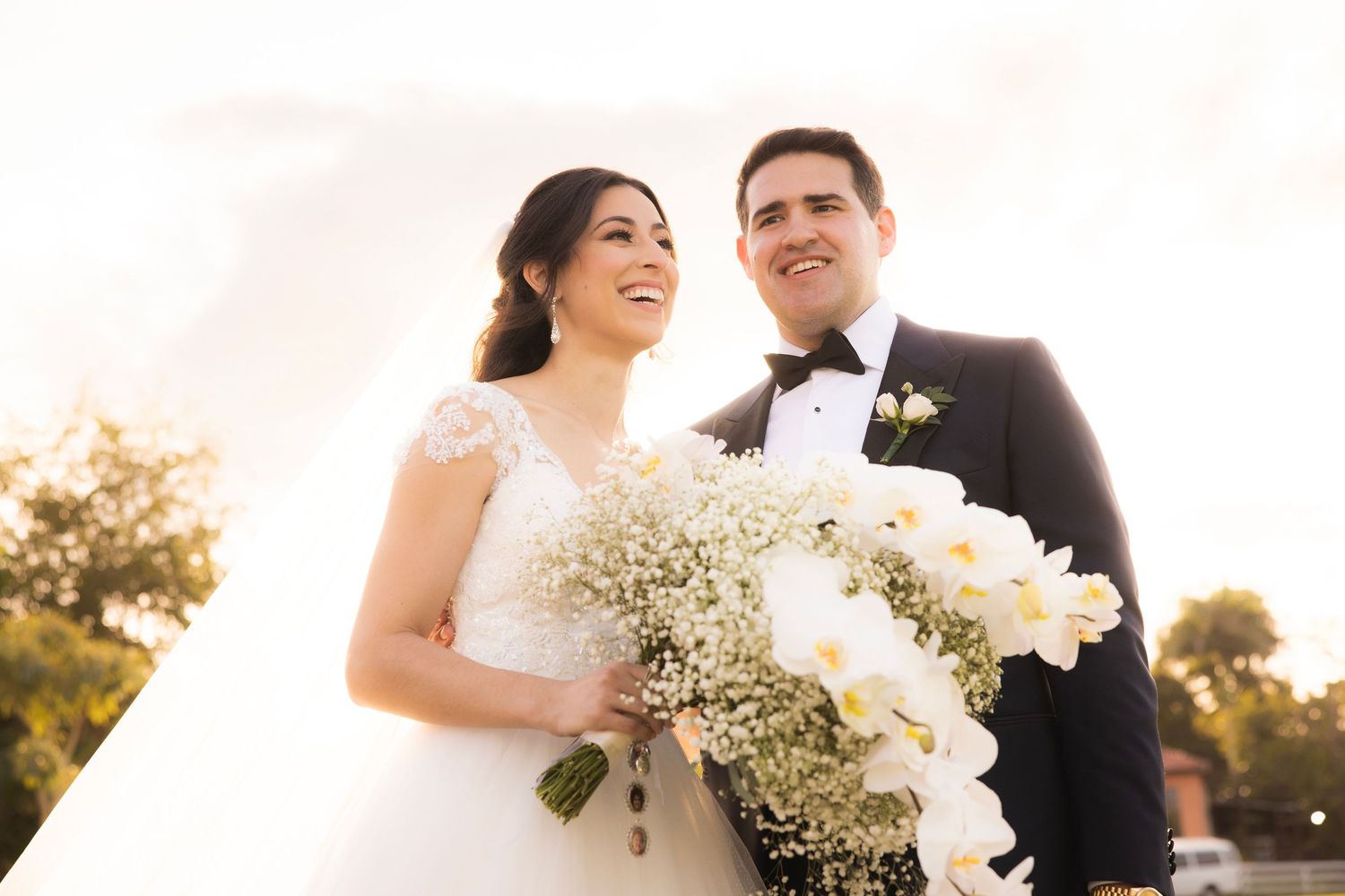 Romantic wedding moment captured in golden afternoon sunlight with white floral bouquet.