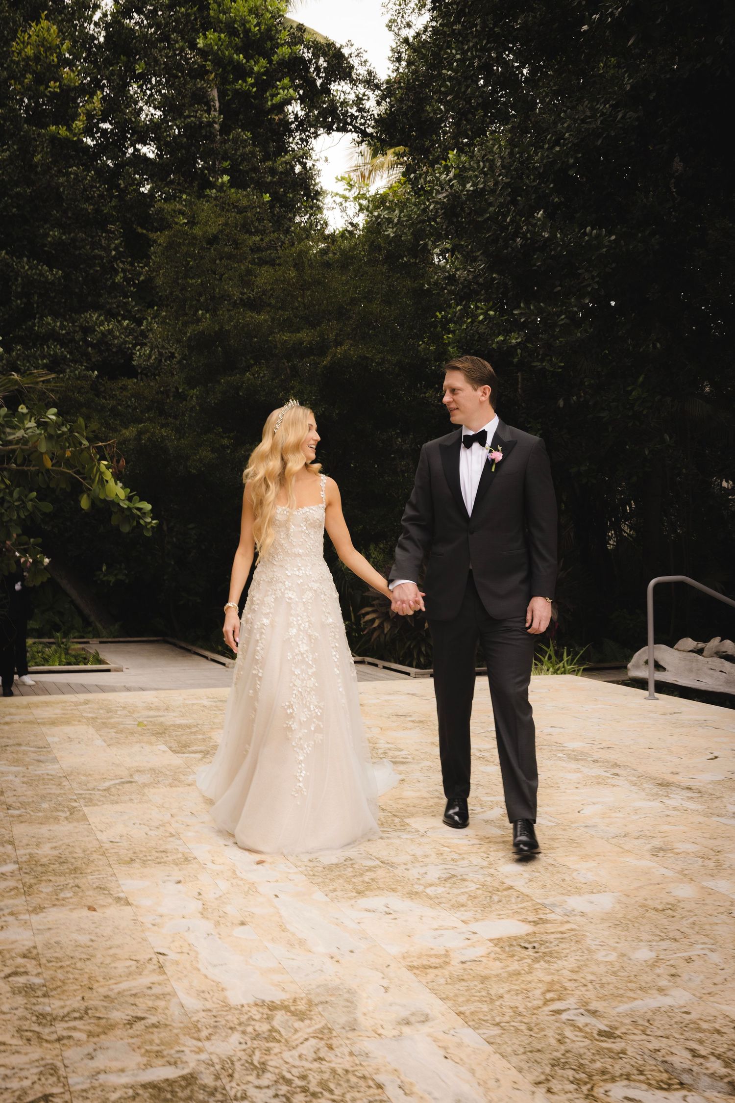 A couple walking hand in hand along a stone path surrounded by lush garden greenery.