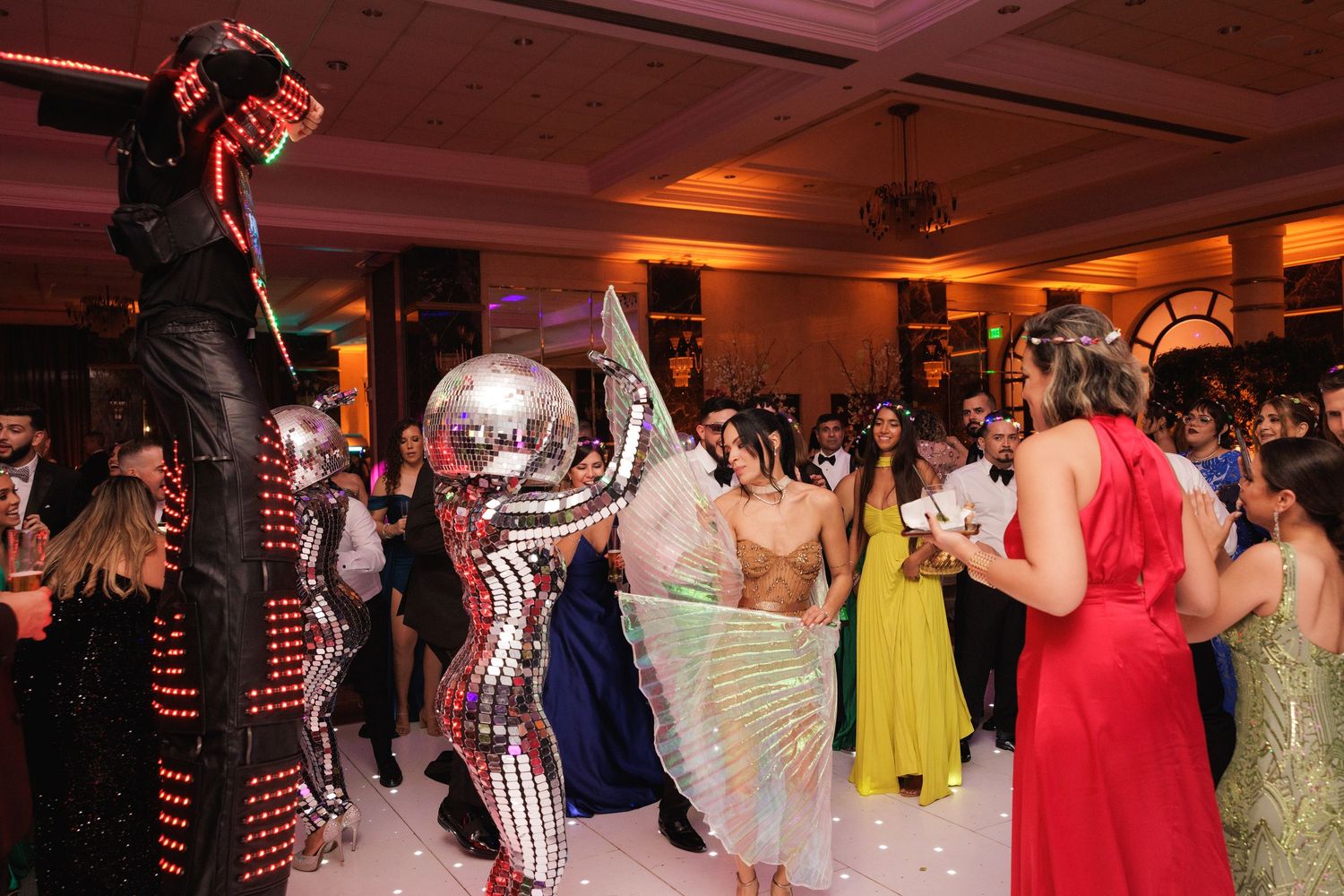 Party guests dance with performers in colorful costumes including a mirror ball suit at an energetic wedding reception.