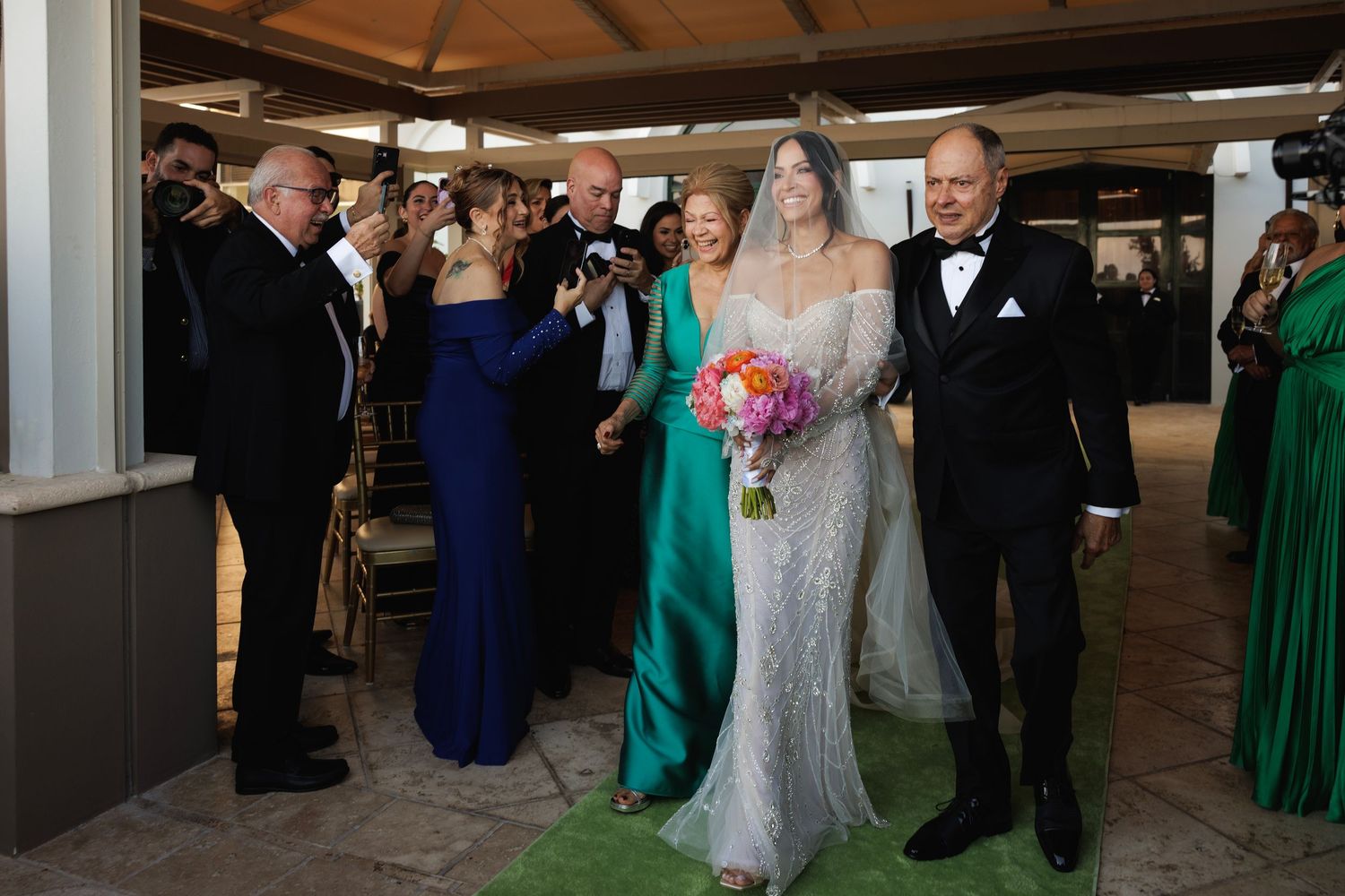 Wedding party gathers indoors with guests wearing elegant evening attire in navy, green and formal black.