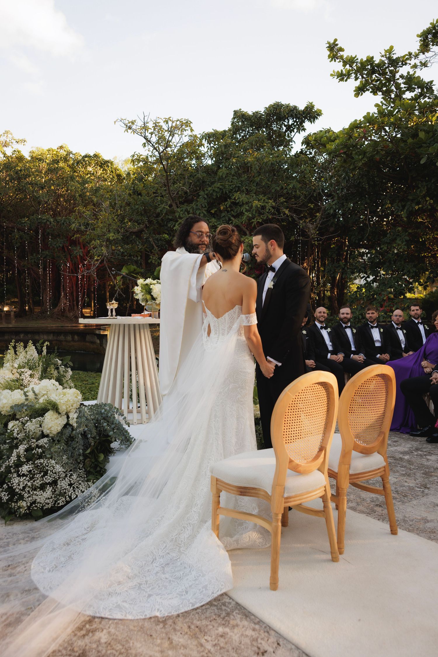 Outdoor wedding ceremony setup with cane back chairs and flowing white dress details.
