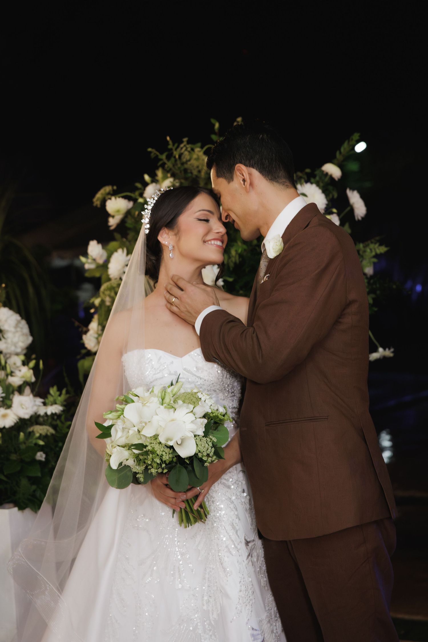 A romantic wedding moment captured under a floral arch with white flowers and soft lighting.