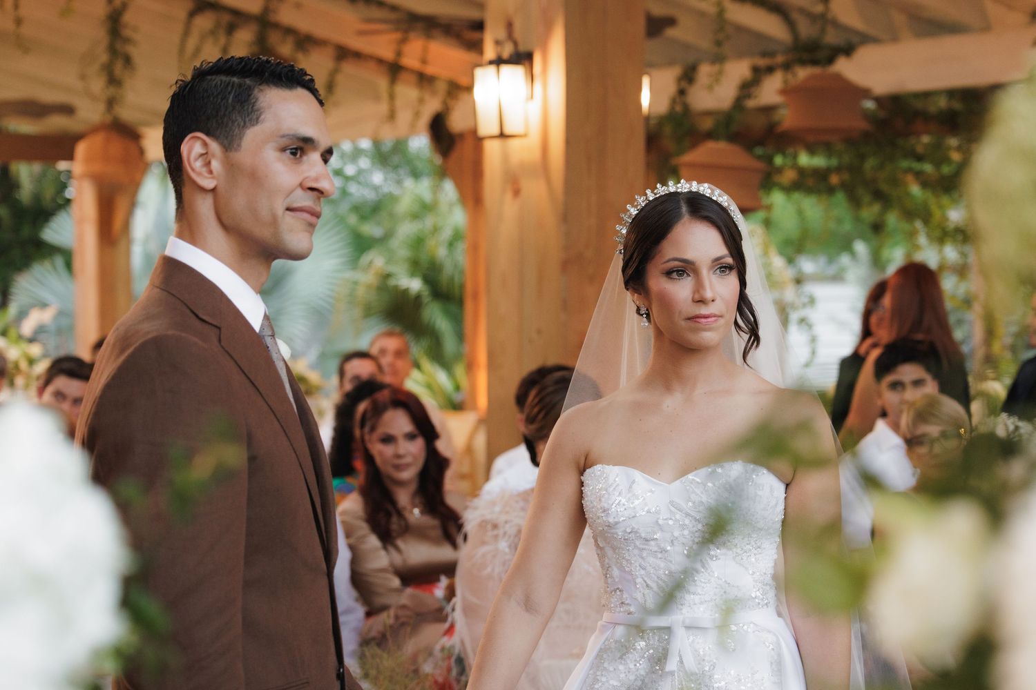 Wedding ceremony taking place under a rustic wooden pavilion decorated with floral arrangements.