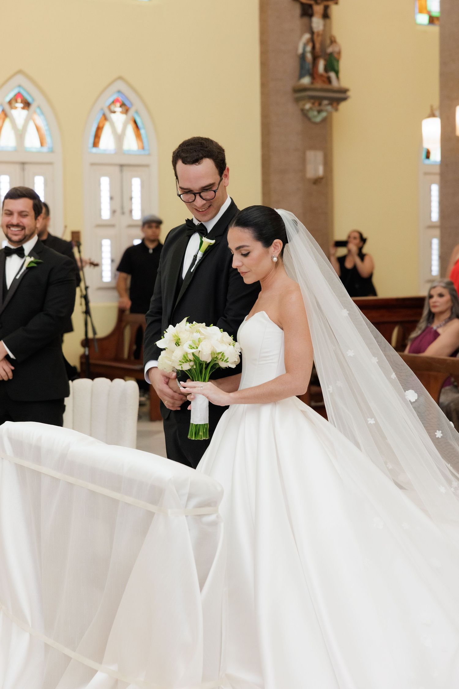 Wedding party gathered in beautiful church with cream walls and gothic architecture.