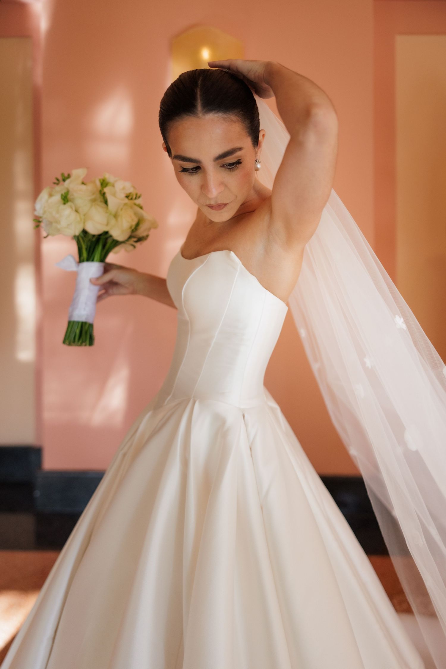 Close-up shots of a white wedding dress with flowing veil against coral-colored walls.