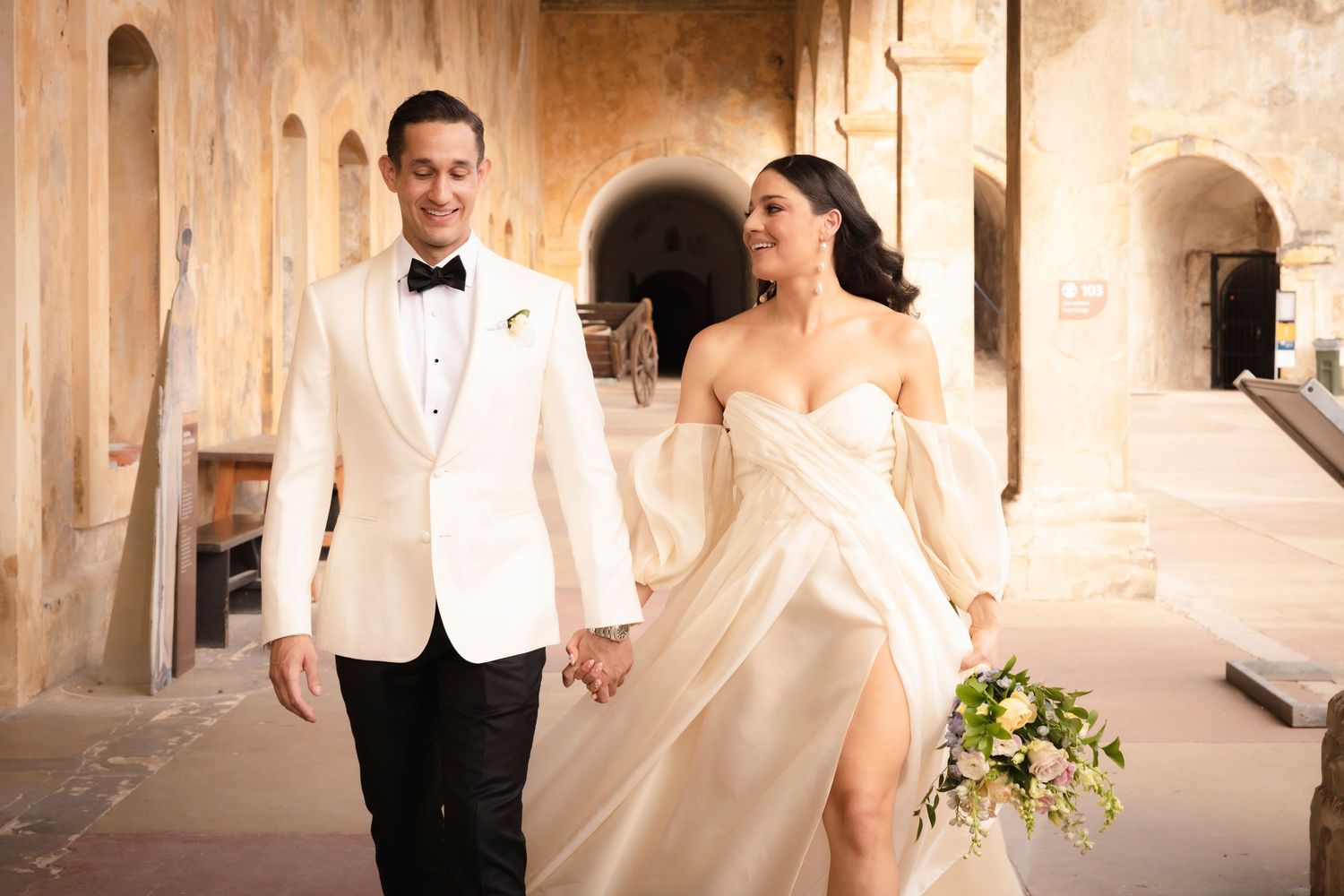 Elegant romantic wedding couple posing together in white under vintage stone archways and columns.