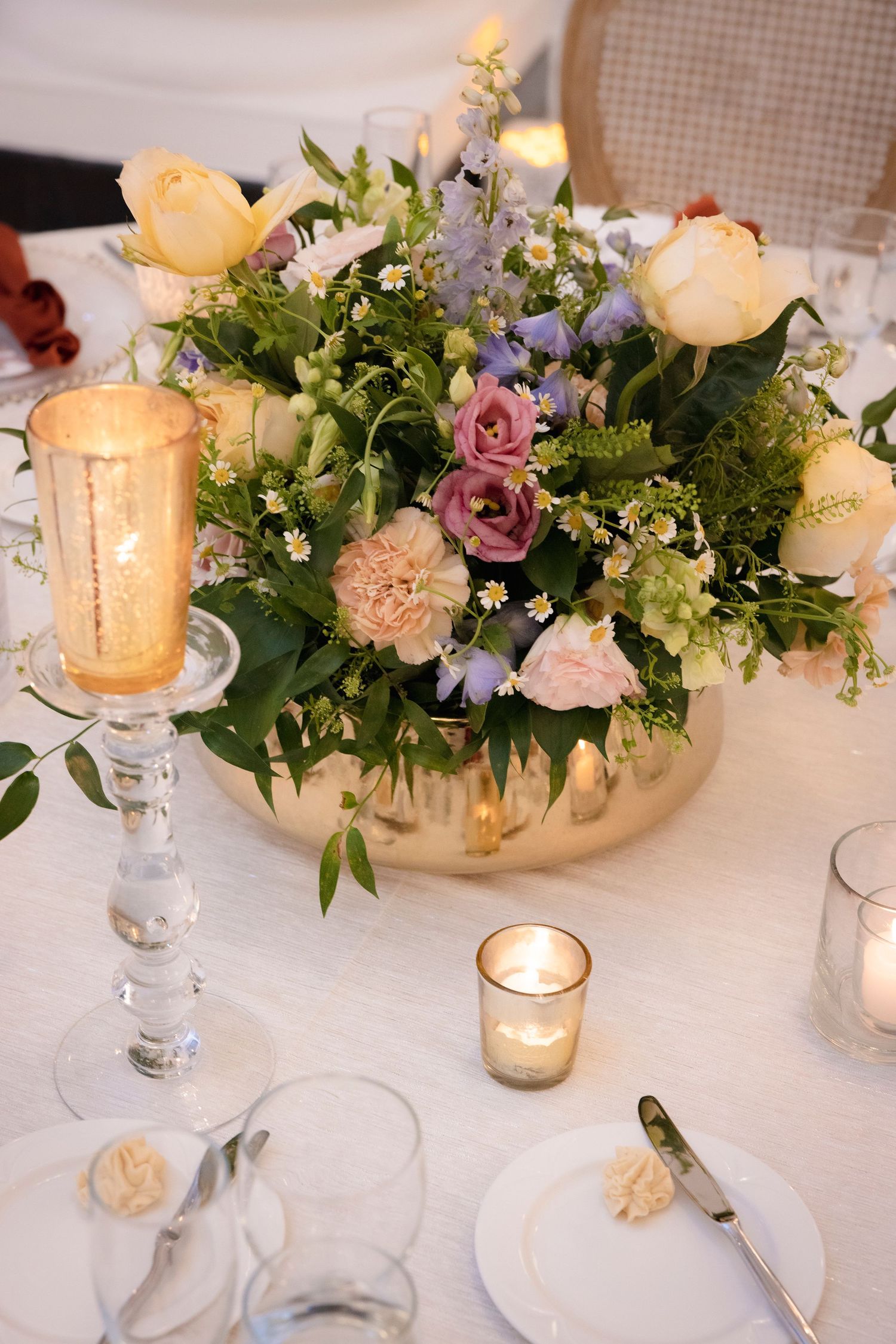 Romantic wedding table setting with floral centerpieces and glowing candles on white linens.