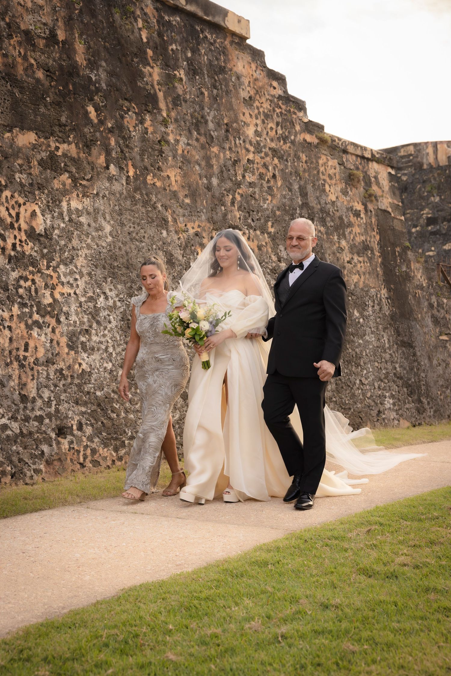 Wedding couple poses along historic stone wall pathway outdoors.
