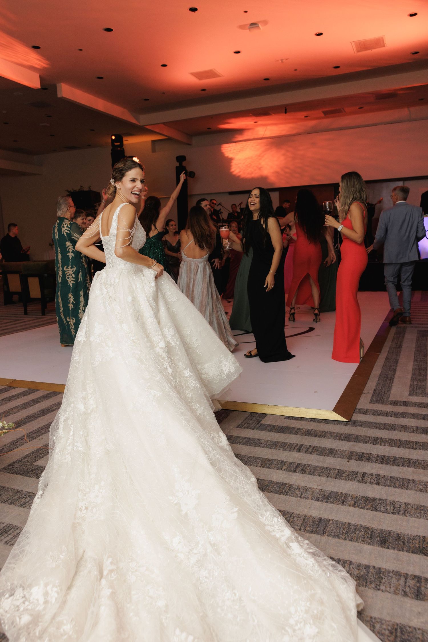 A bride in a flowing white lace ballgown twirls and dances gracefully on a geometric patterned ballroom floor.
