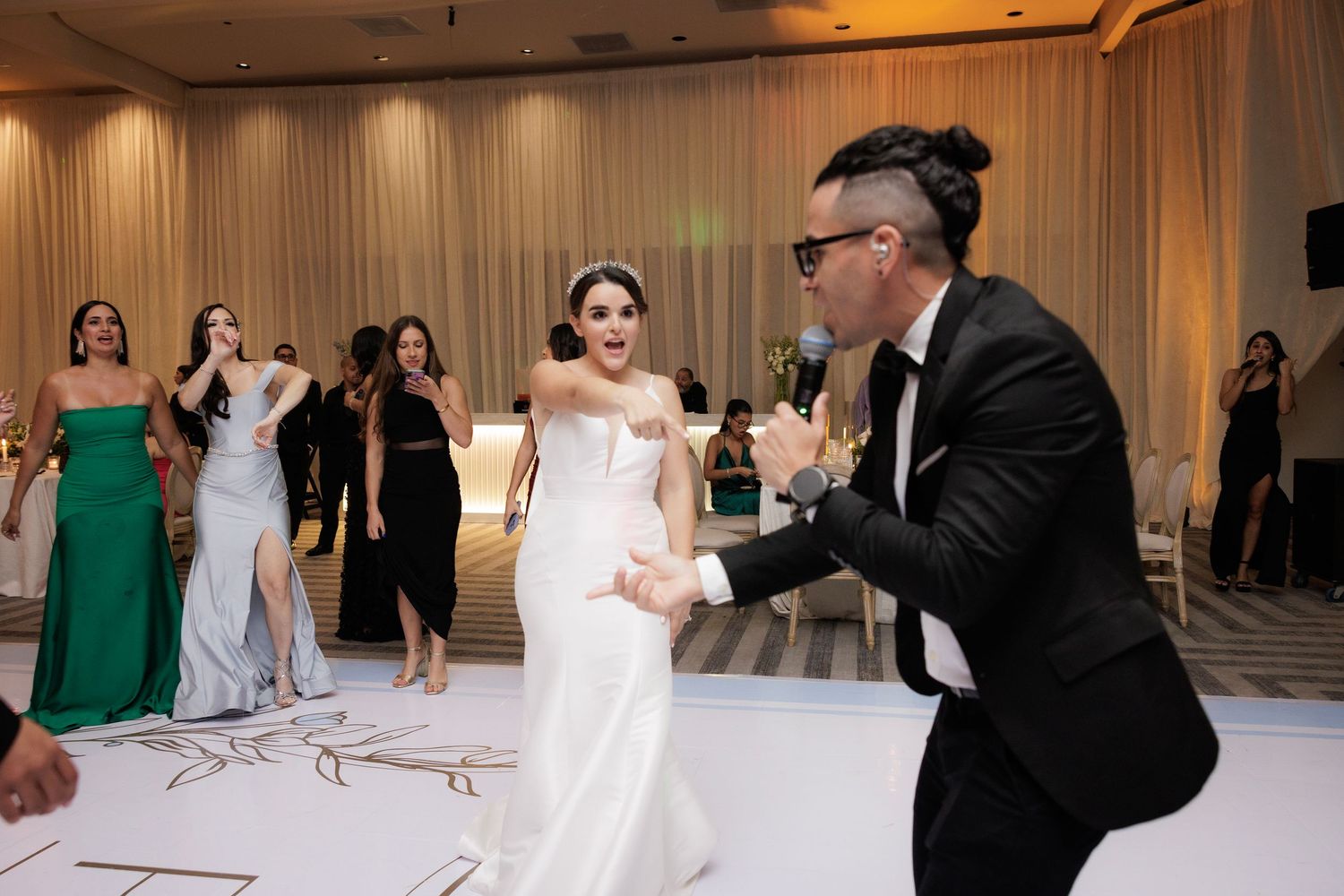 Wedding guests enjoying the dance floor during a reception in an elegantly lit indoor venue with white decor.