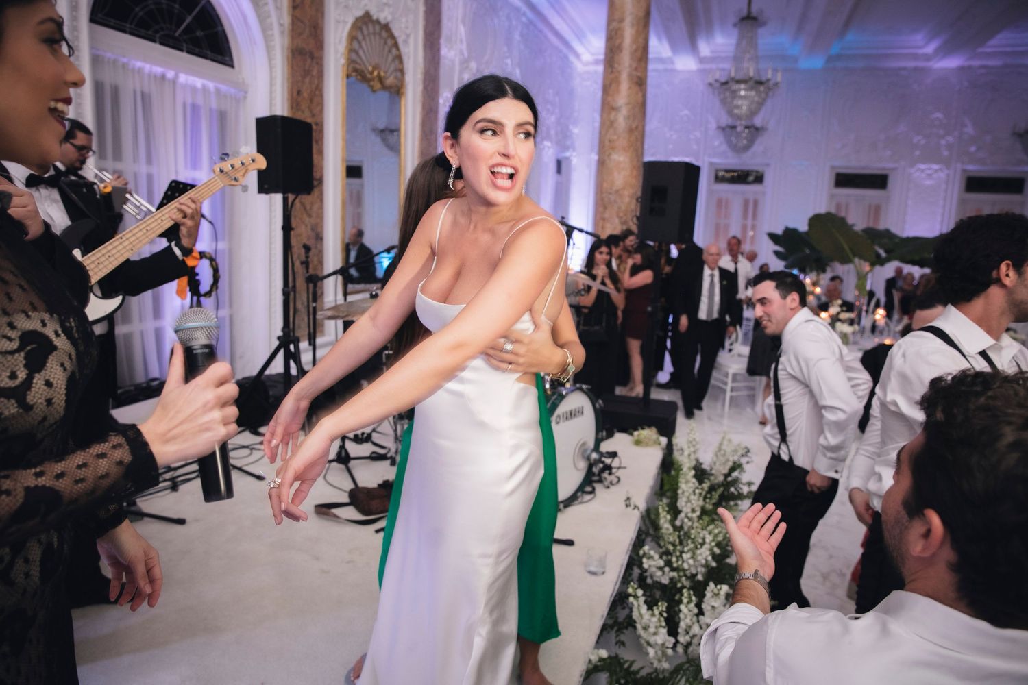 Lively wedding reception crowd dancing and celebrating in an ornate white ballroom venue.