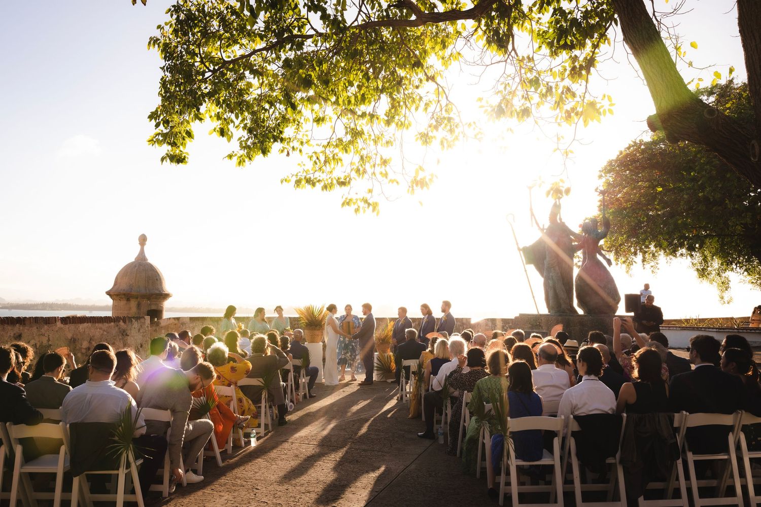 Outdoor wedding ceremony setup with wooden chairs against a sunset background.
