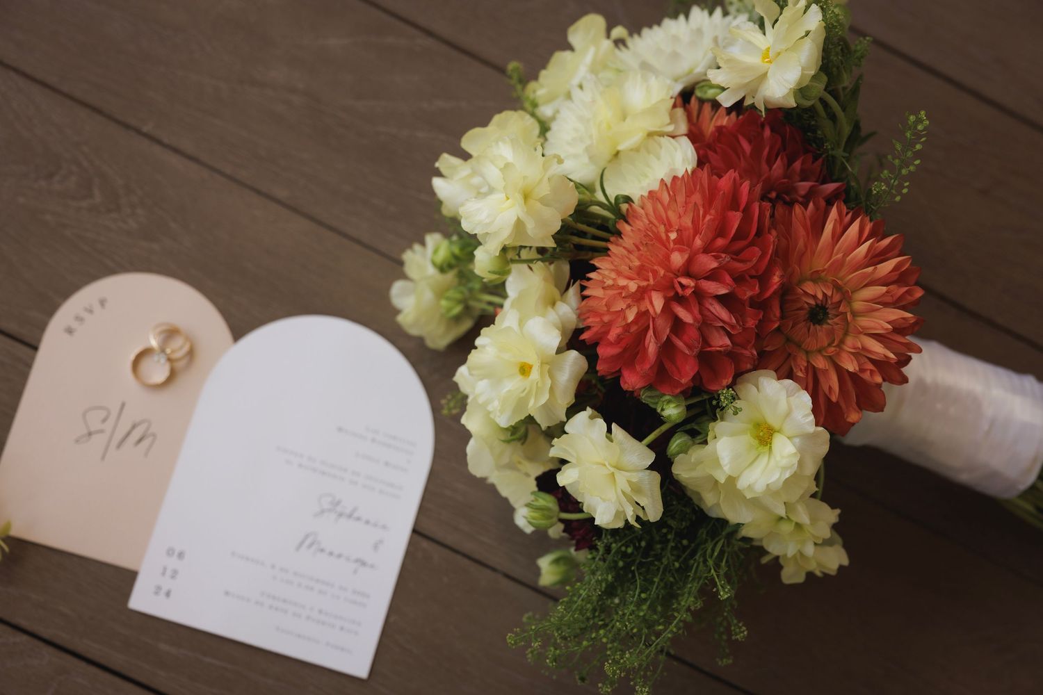 Wedding details with peach and ivory floral arrangements next to elegant invitation cards on wooden surface.