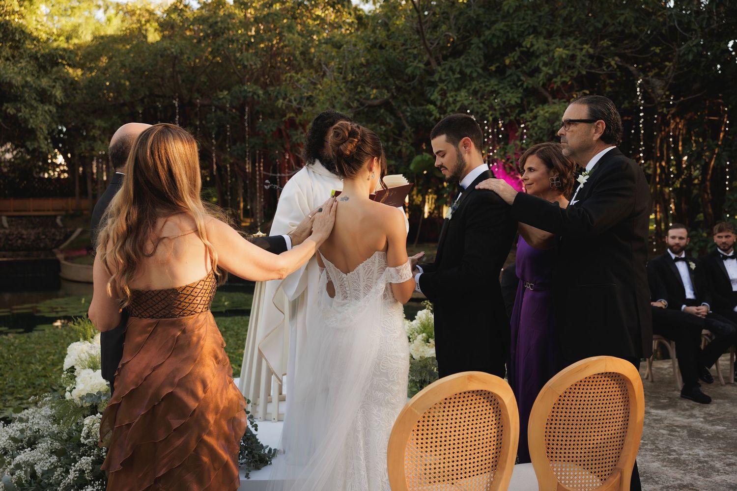 Outdoor garden wedding ceremony with wicker chairs and floral decorations at sunset.