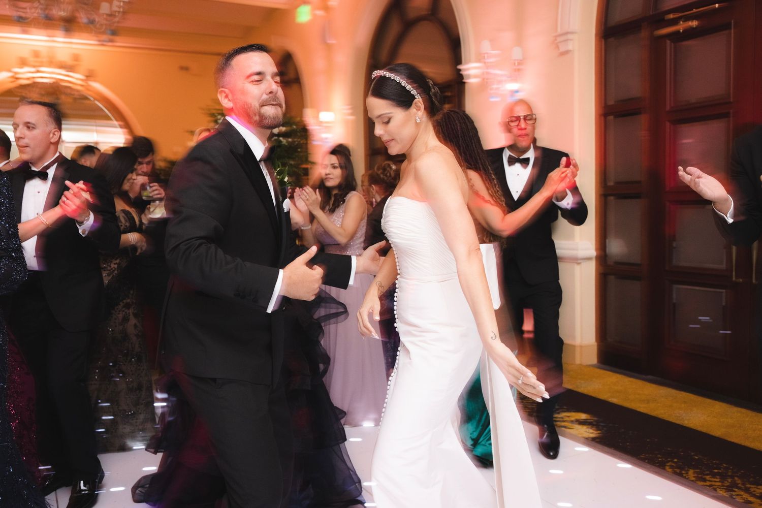 Couples dance during a wedding reception in a warm-lit banquet hall decorated for a formal celebration.