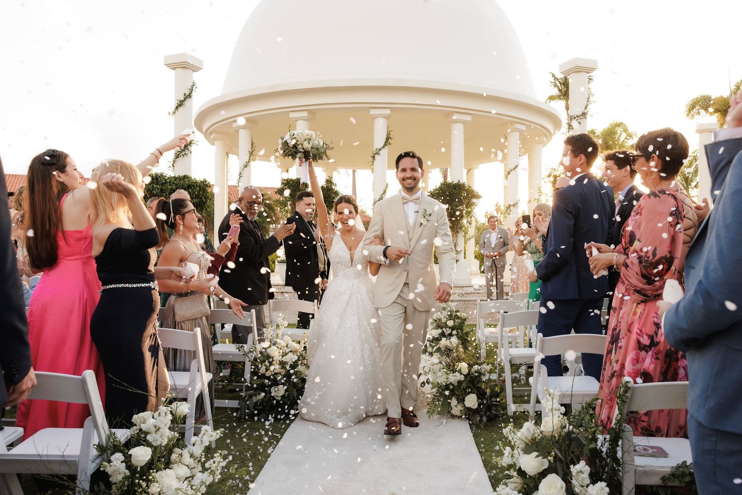 A romantic outdoor garden wedding ceremony with guests seated under white tents and floral arrangements.