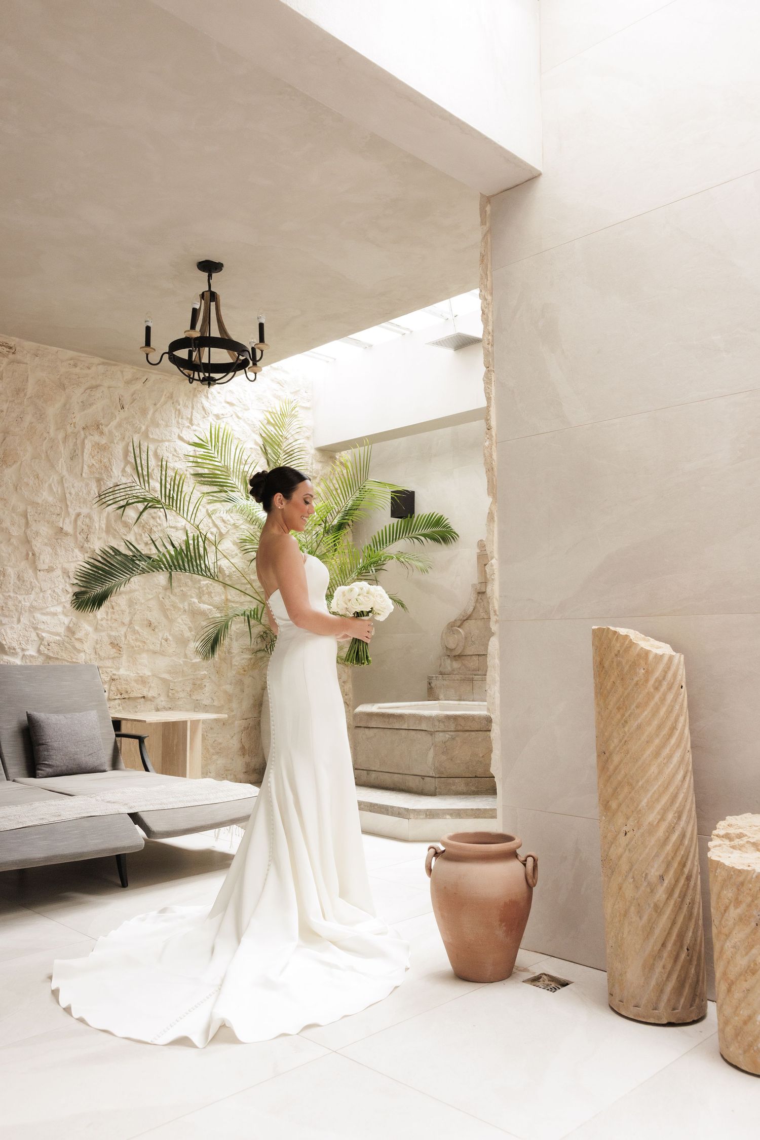 Wedding dress captured in bright white room with stone walls and tropical plants.
