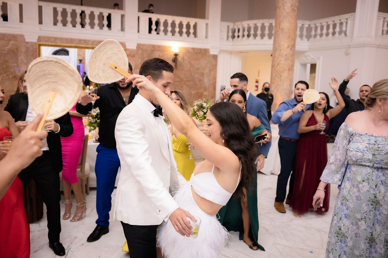 Wedding reception guests dance and celebrate together on a dance floor in formal attire during an indoor event.