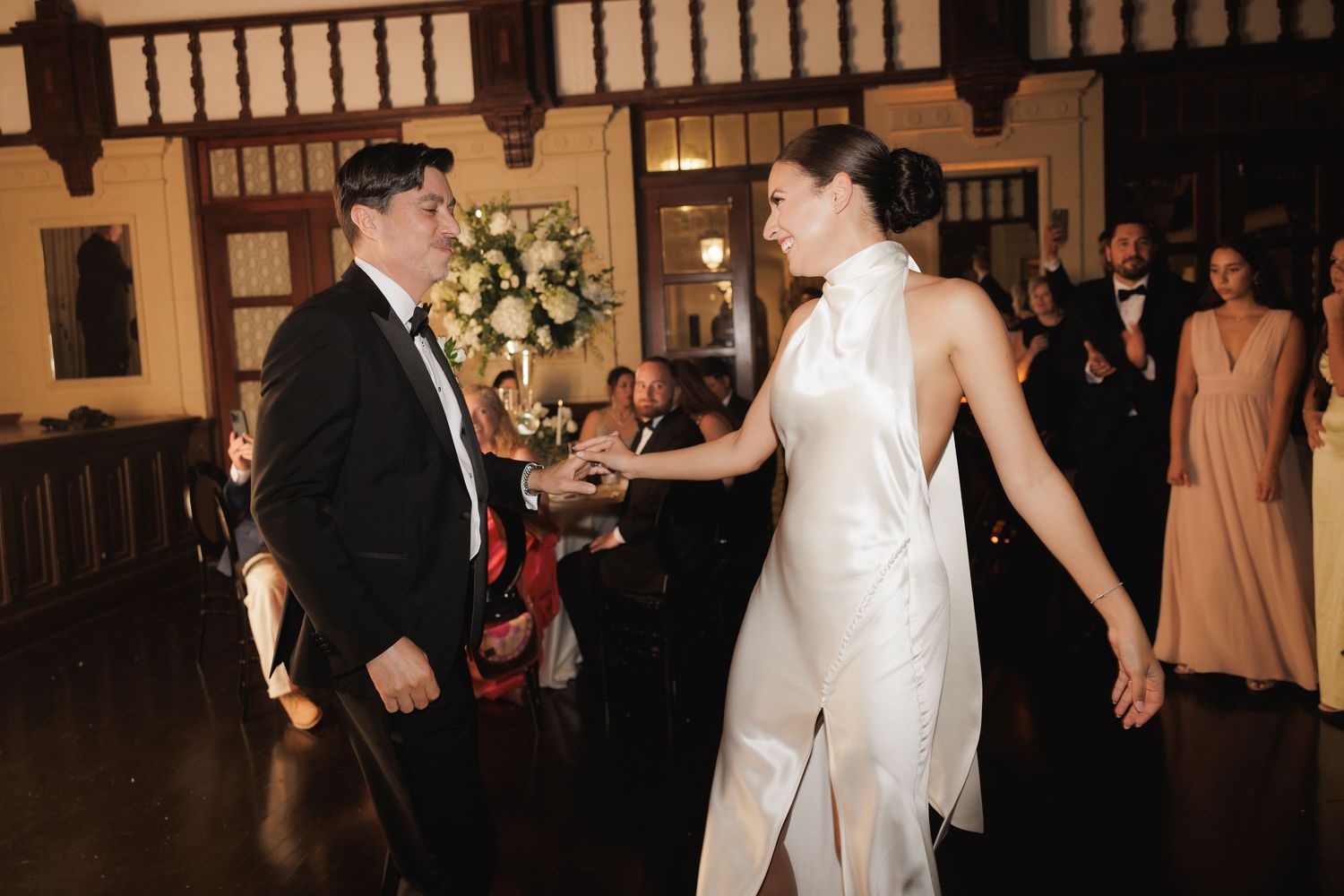 Couple sharing their first dance at a wedding reception in a dimly lit ballroom with elegant decor.