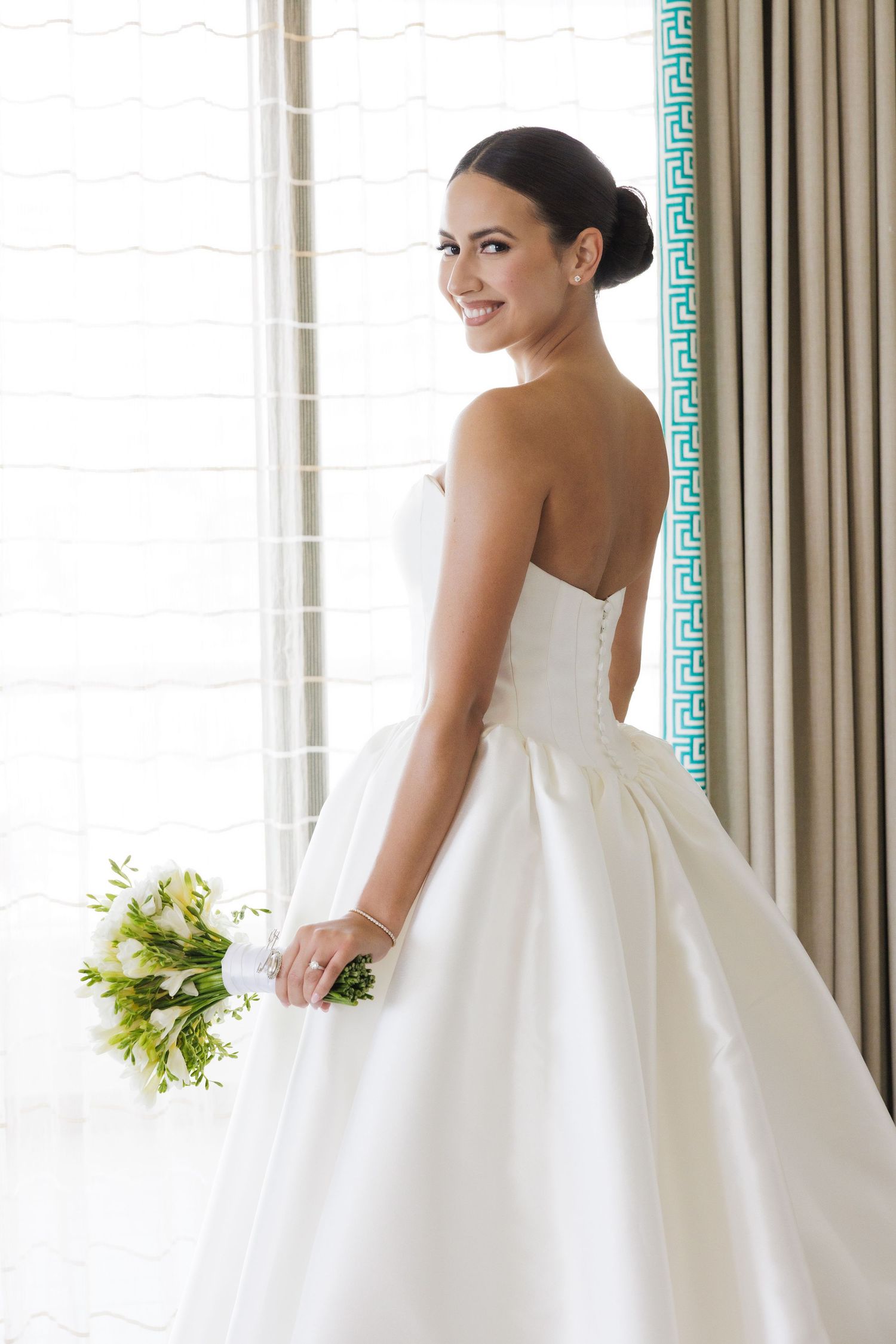 Elegant white wedding gown with full skirt photographed against bright window light.