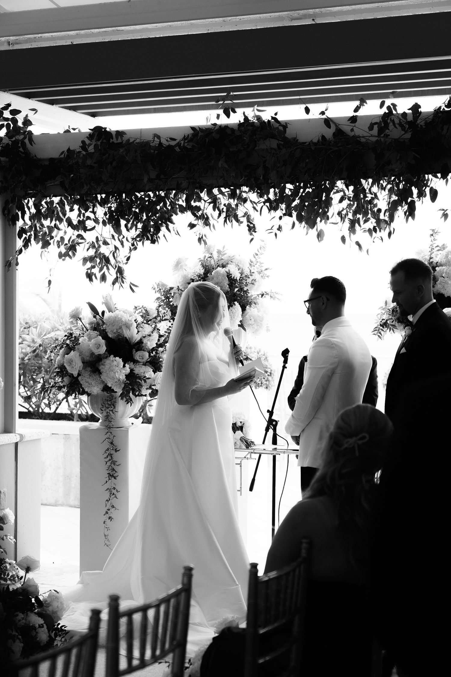 A black and white silhouette of a wedding ceremony with floral arrangements and guests in attendance.