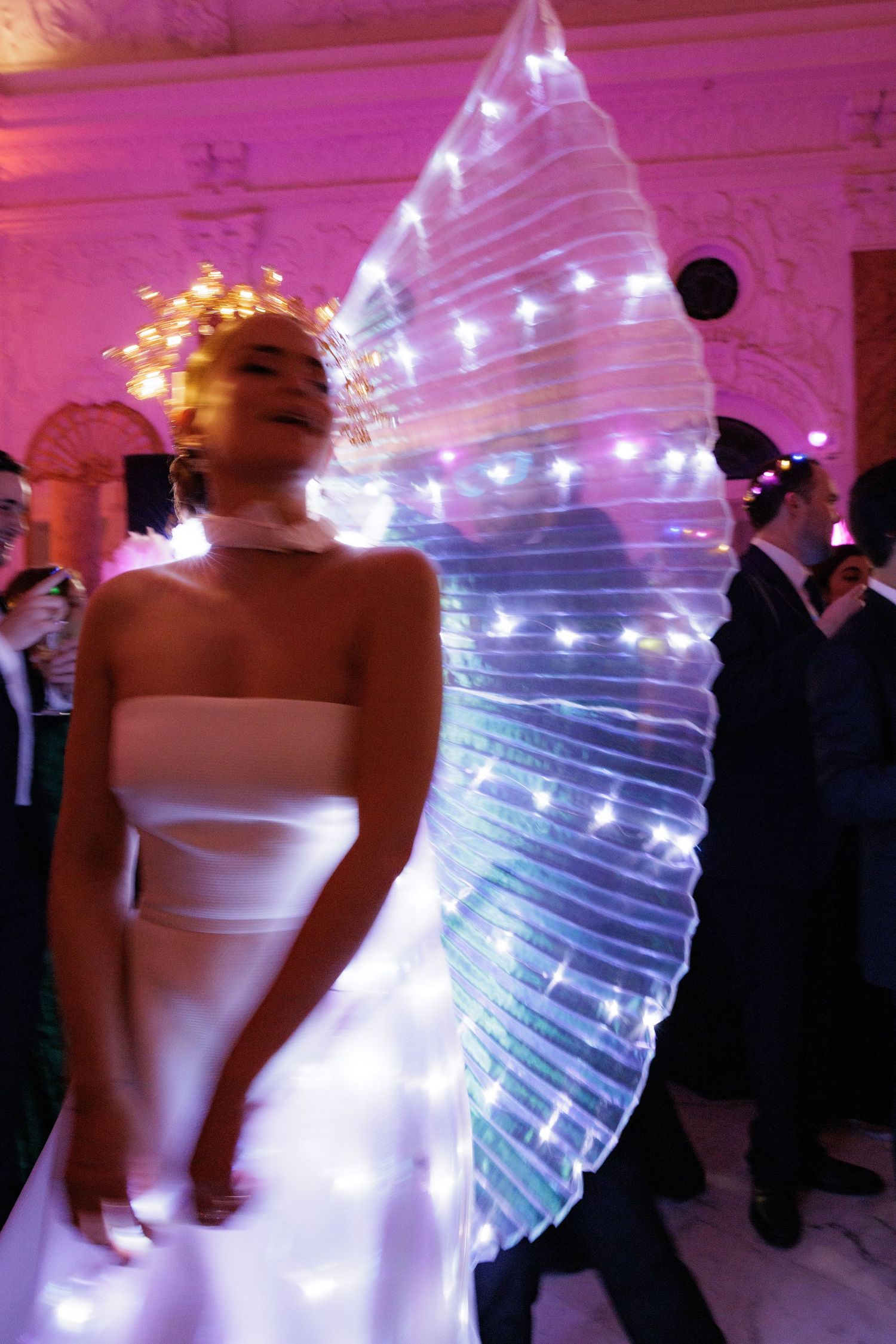 Multiple exposure shot shows ethereal dance performance with flowing white dress and LED light effects in pink venue.