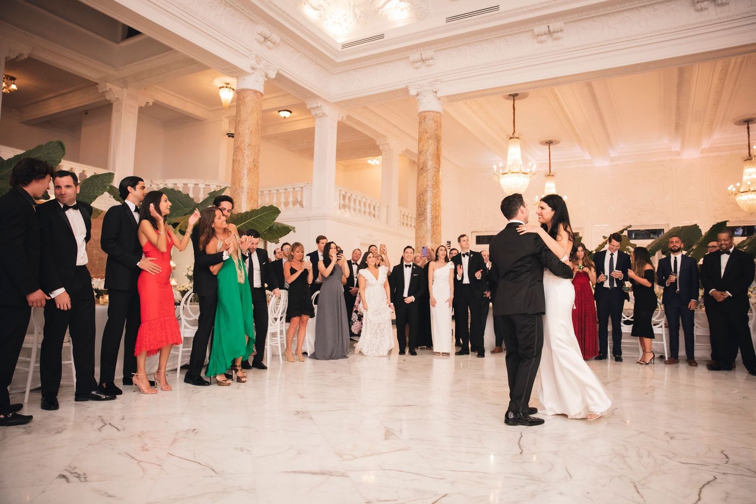 Spacious white ballroom filled with wedding guests dancing at an evening celebration.