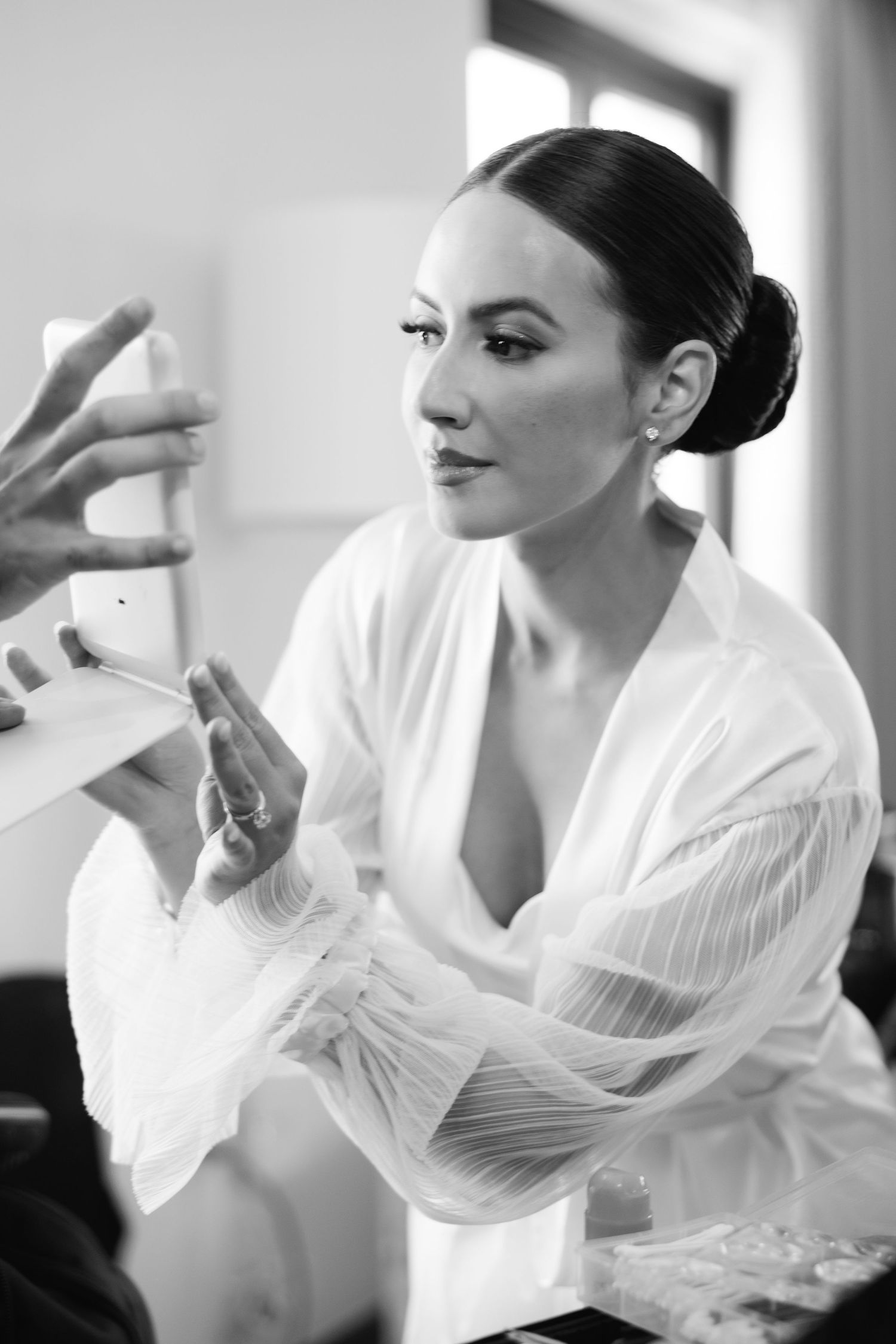 Black and white portrait of bride getting ready in elegant white robe with sleek updo.
