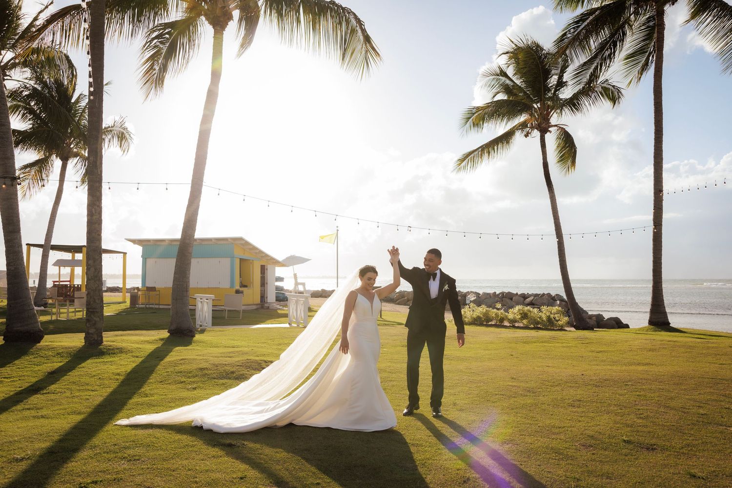 A beachfront wedding ceremony in Hawaii with palm trees swaying in the golden sunlight by the ocean.