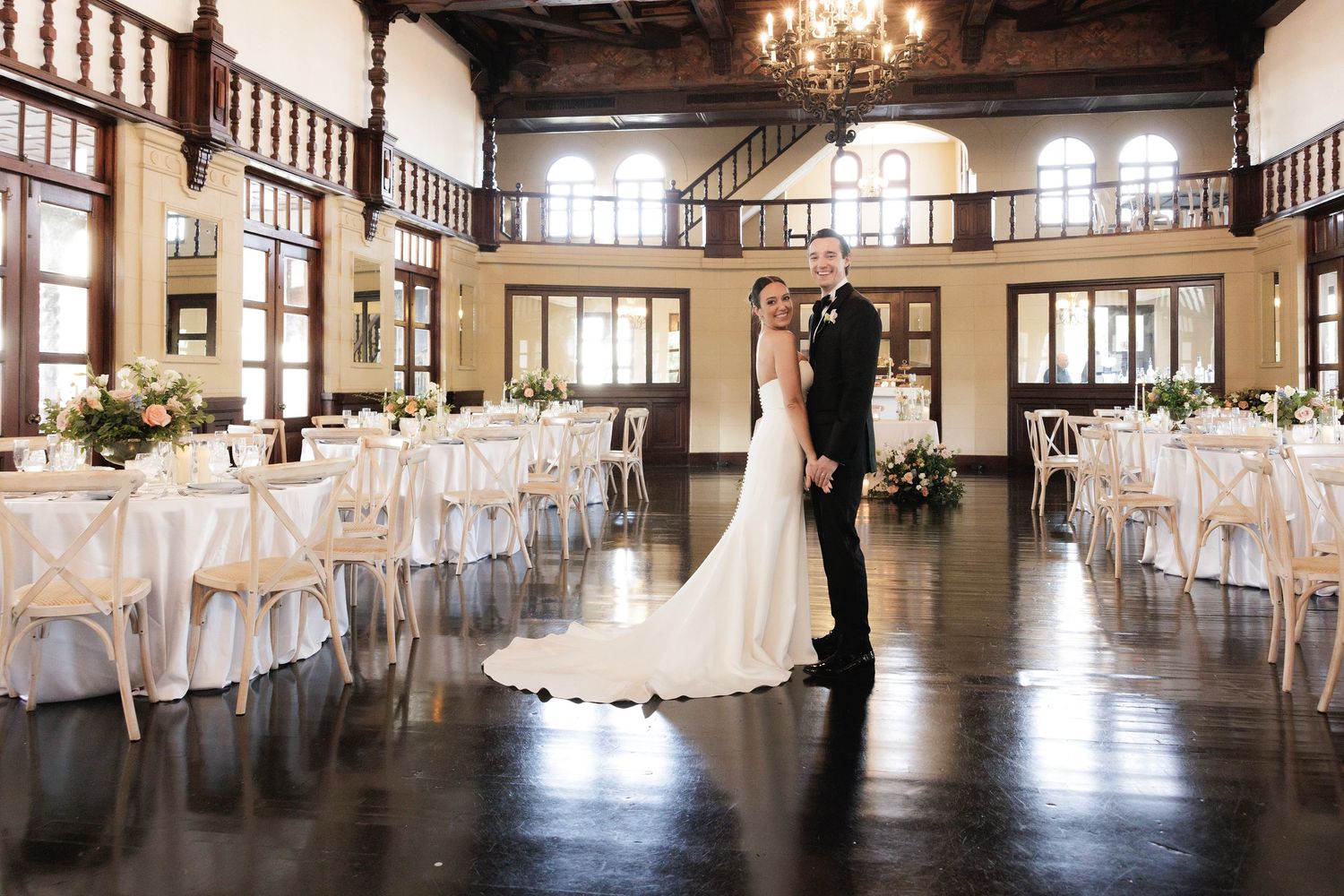 A large rustic event venue with vintage chandeliers and white dining tables set for an elegant reception.