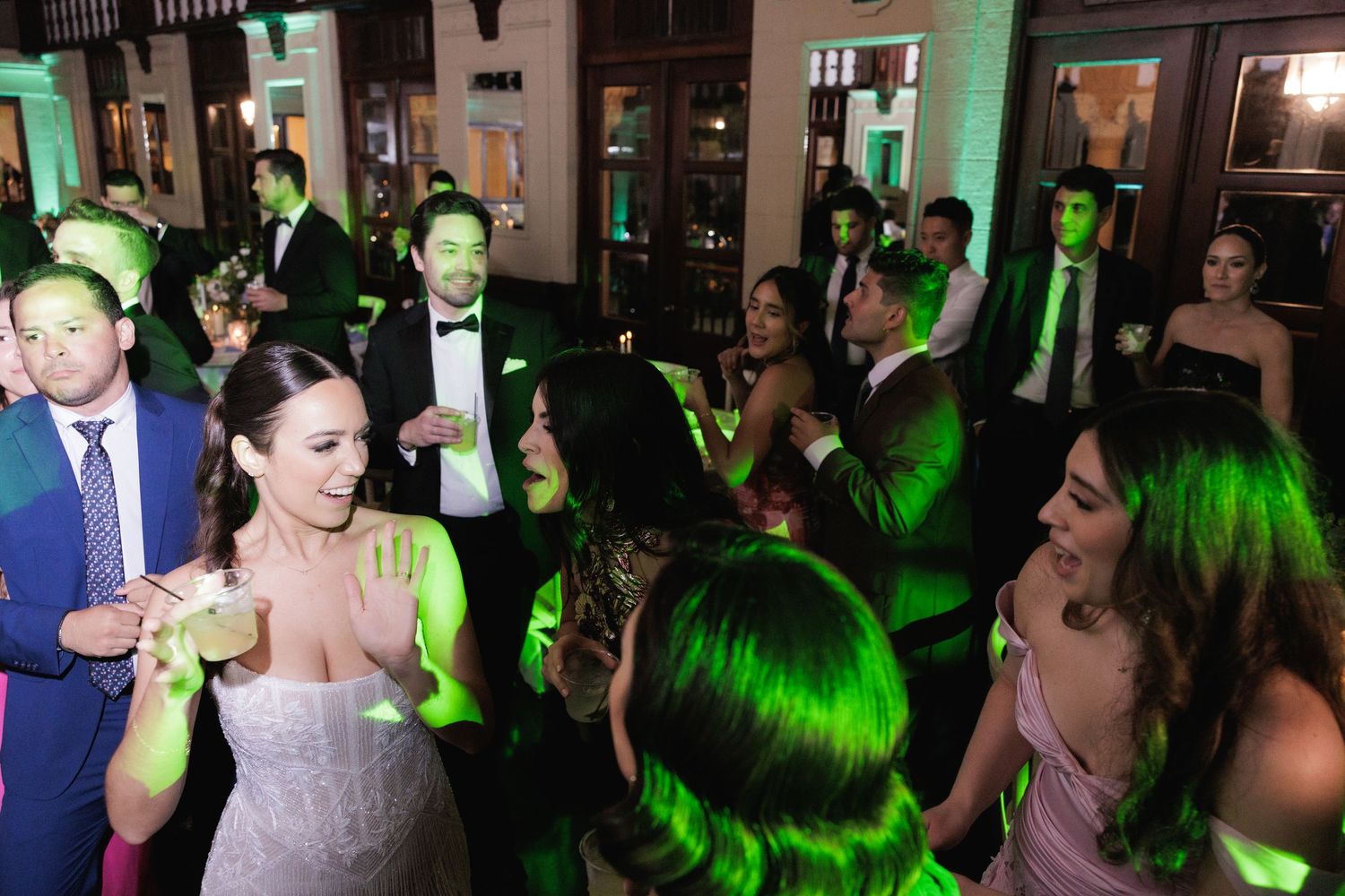 A lively wedding reception dance floor with green lighting as guests celebrate and dance together.