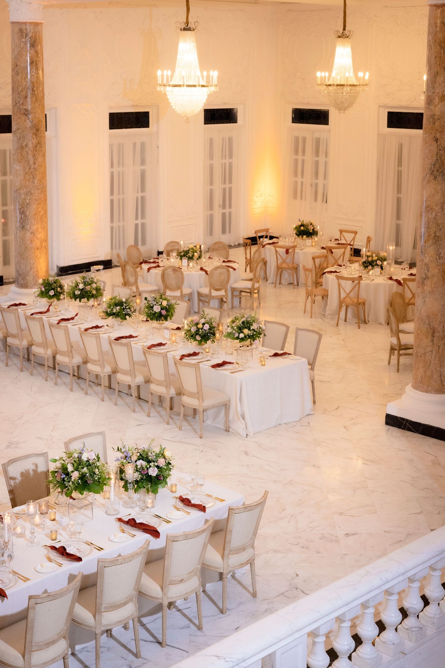 Elegant wedding reception venue with crystal chandeliers and long tables adorned with white linens and floral centerpieces.