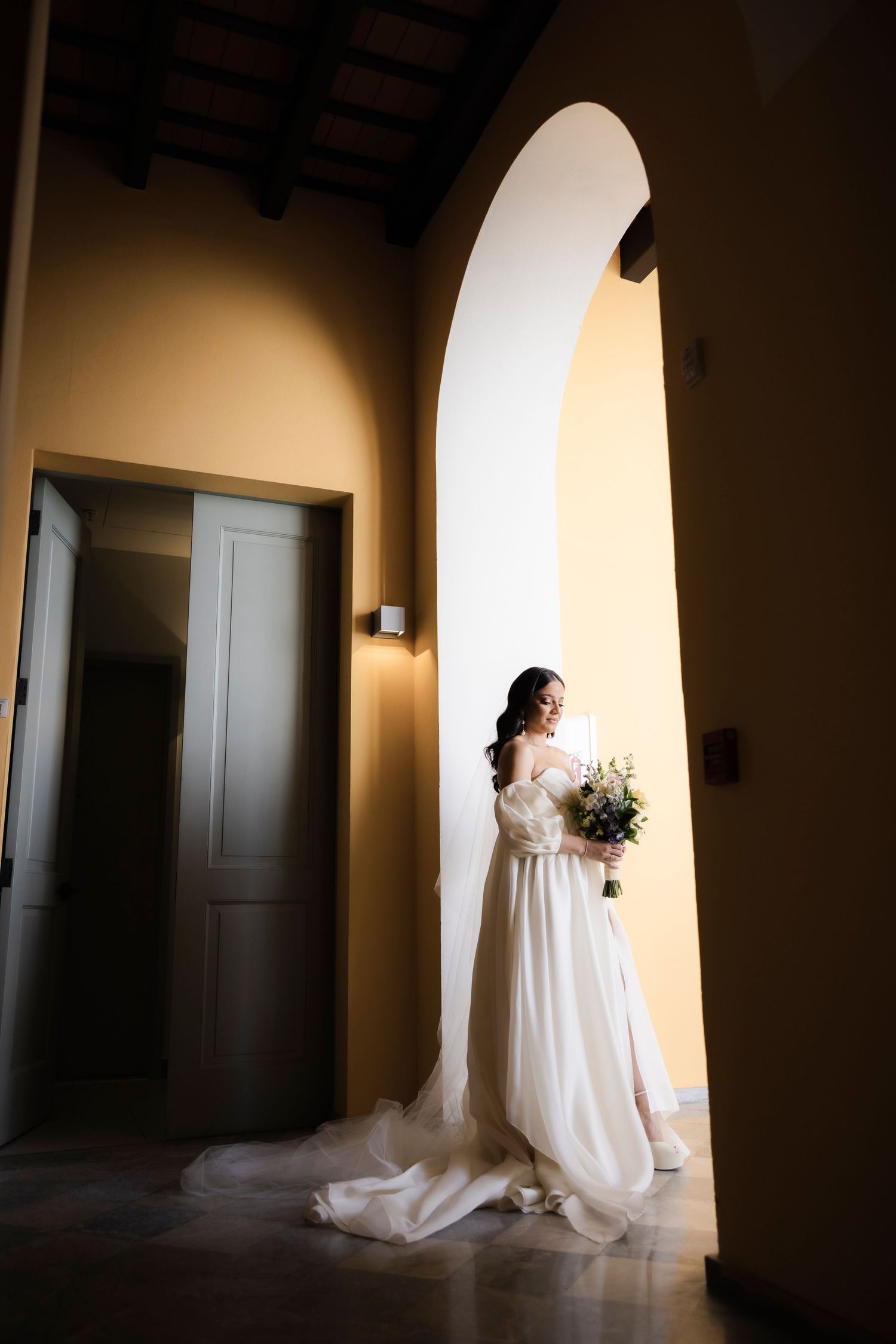 Wedding dress silhouette against arched hallway with dramatic lighting and shadows.