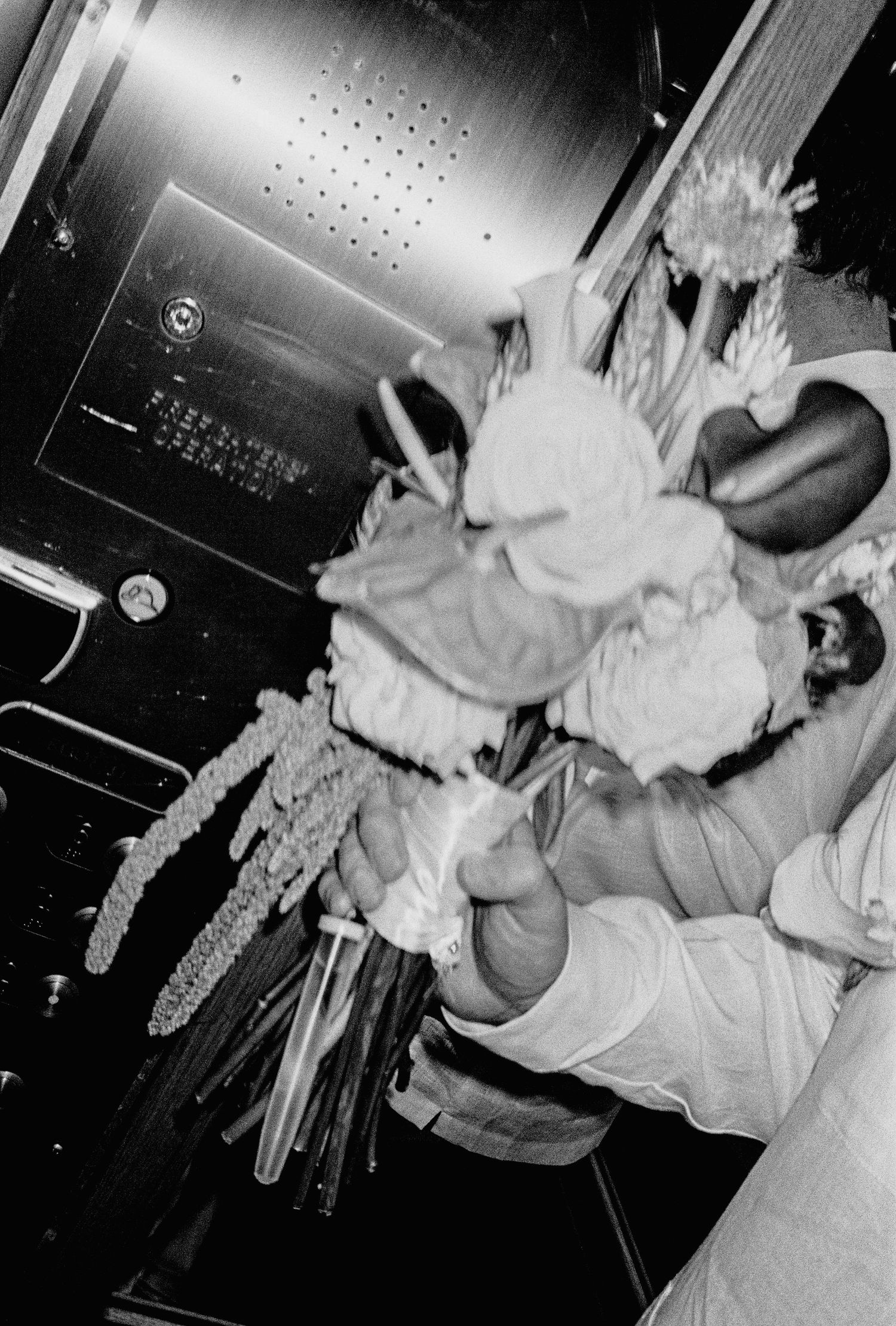 Black and white photo of a bride holding a lush wedding bouquet with roses and greenery in an elevator.