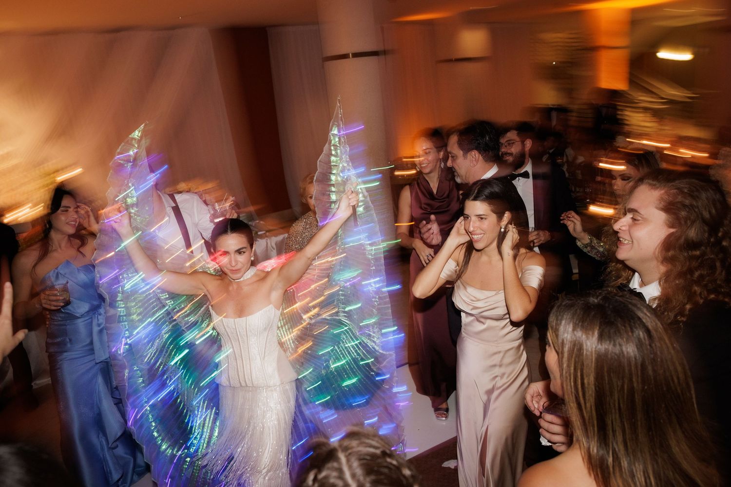 Wedding reception dance floor moment with iridescent wings creating a magical light show.