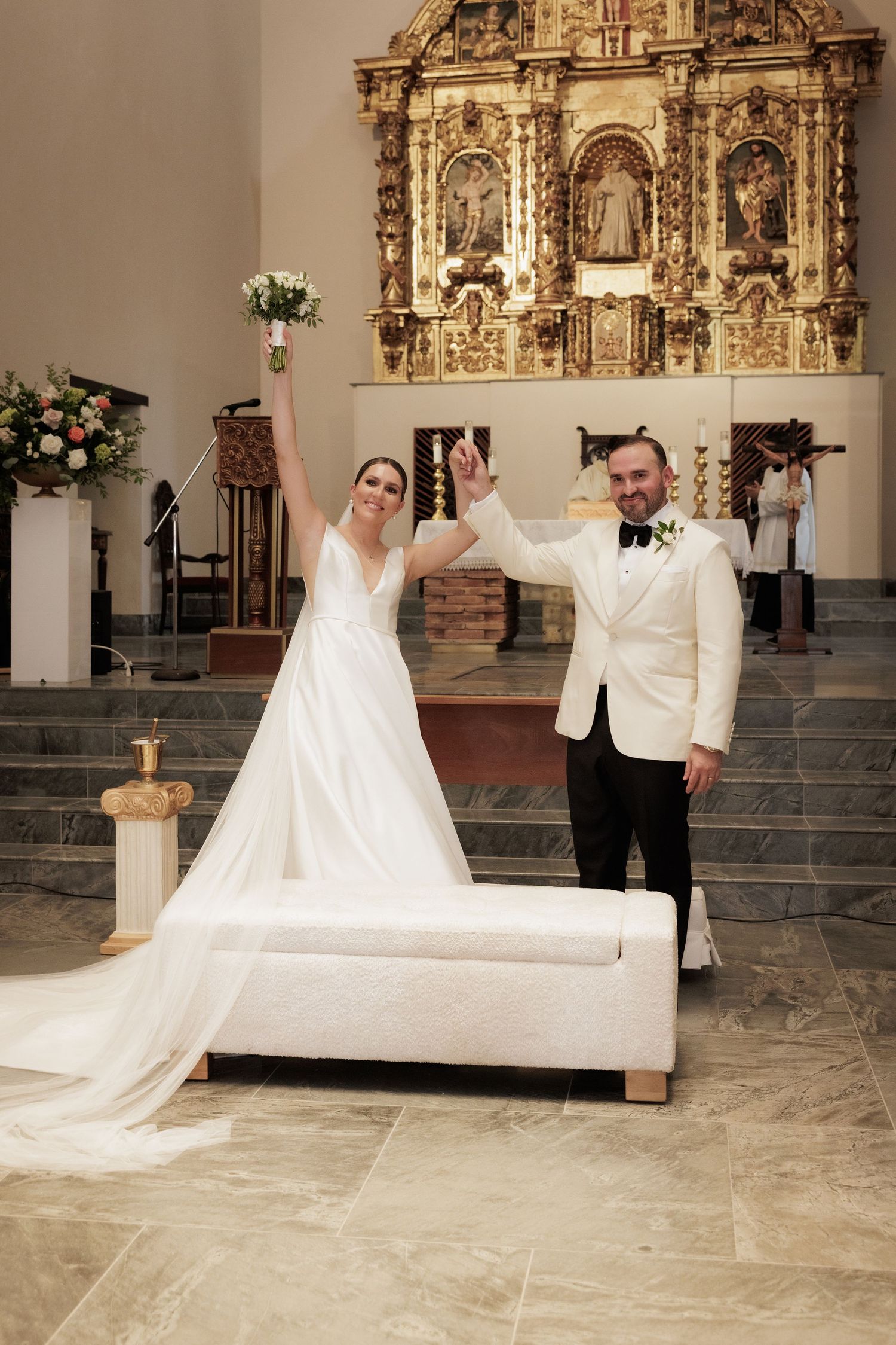 Wedding couple posing in front of an ornate golden altar in a church.