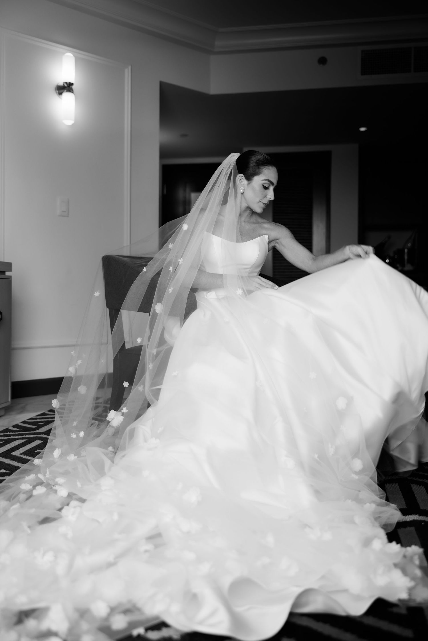 Black and white photo of a bride in a flowing ball gown and veil, twirling elegantly in a hotel room.