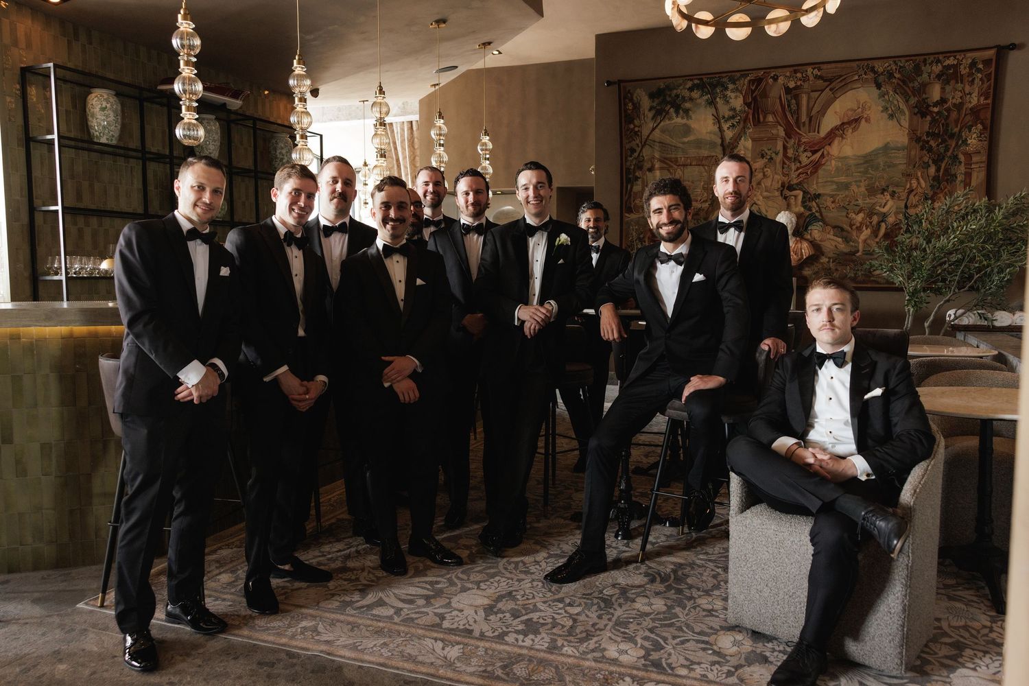 Groomsmen dressed in classic black tuxedos pose together in an elegantly decorated room with ornate furnishings.