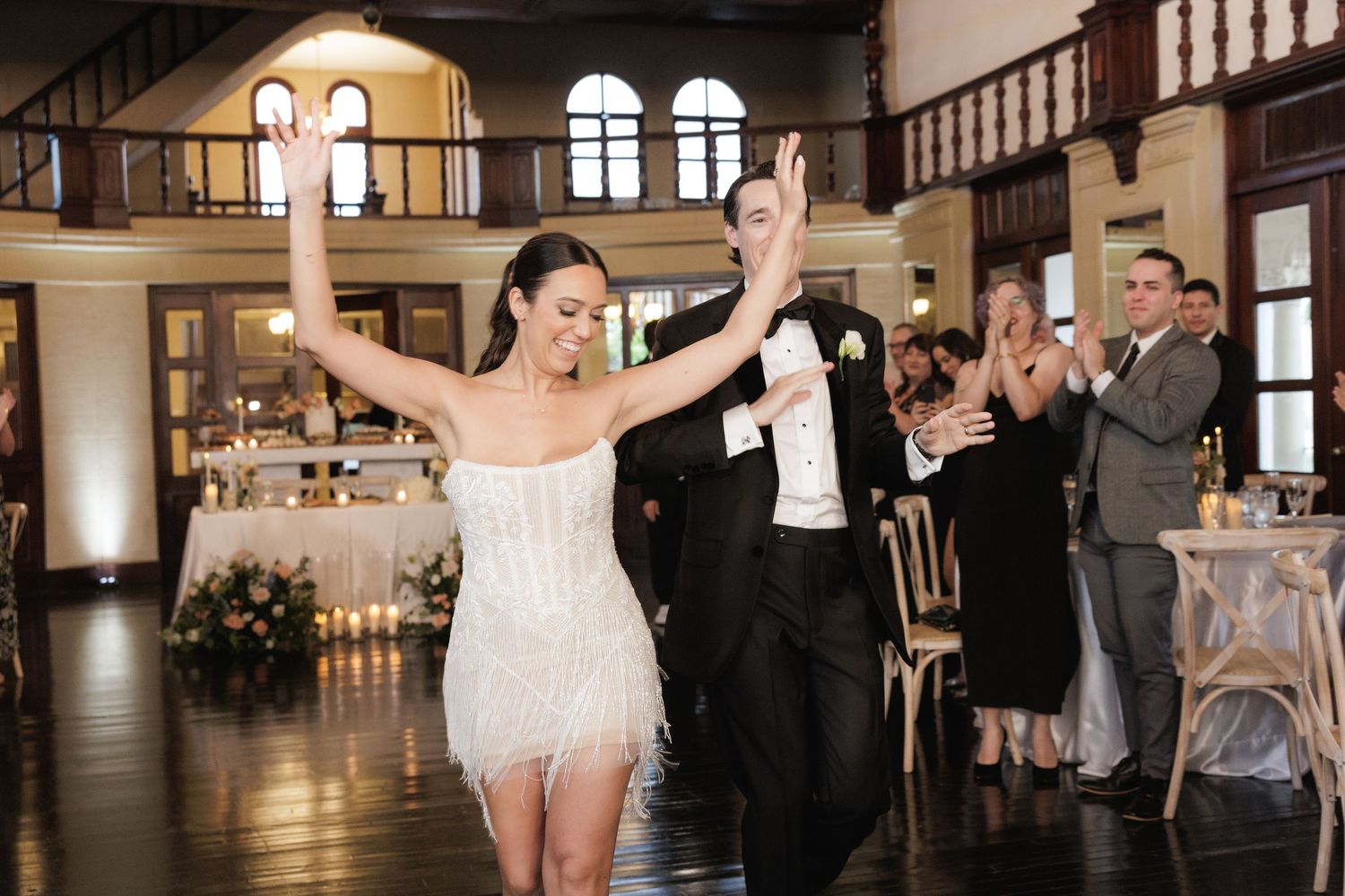 Dancers perform an elegant ballroom routine in a grand historic venue with exposed wooden beams and chandeliers.