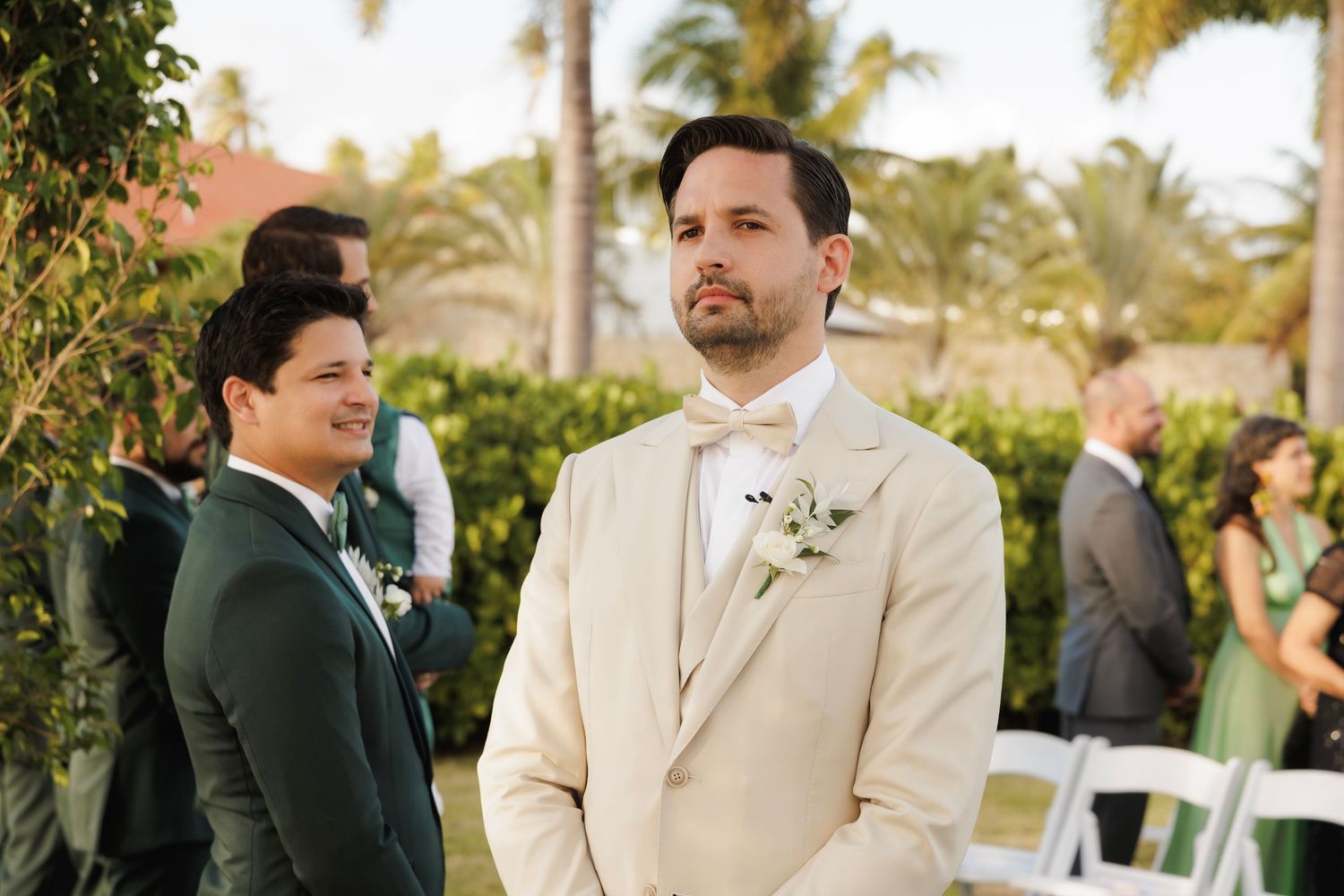 Wedding guests enjoying conversation during an outdoor reception in a tropical garden setting with palm trees.