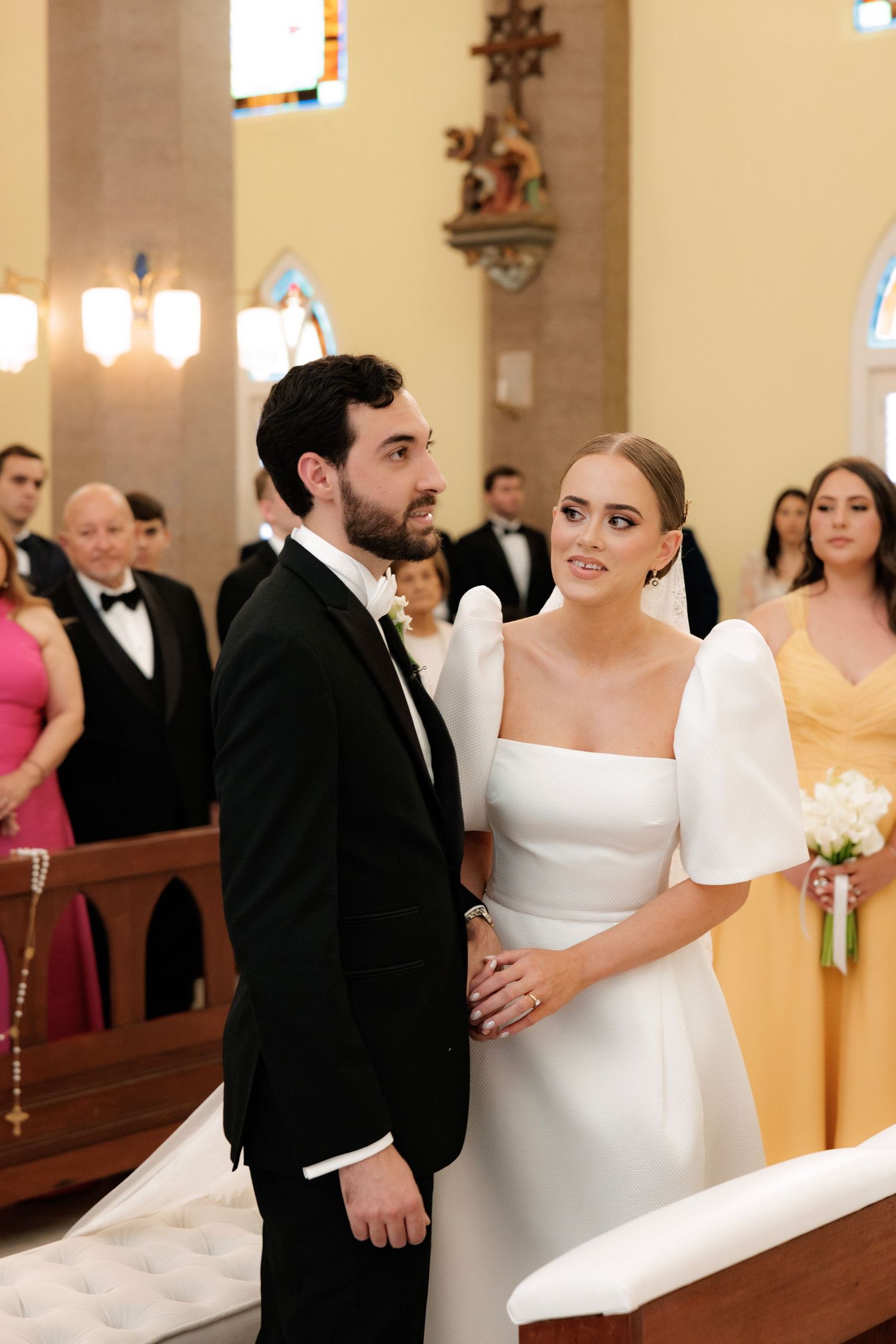 A couple exchanges glances during their traditional church wedding ceremony surrounded by guests.
