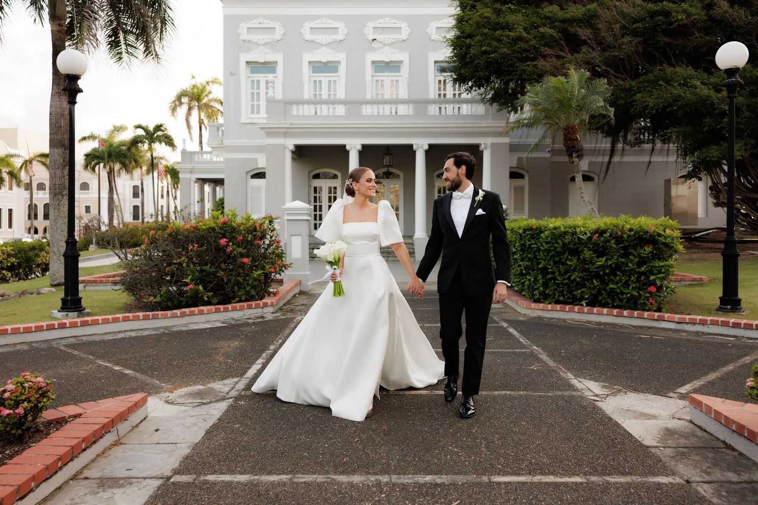 Wedding couple and attendant walk along a palm-lined path on their special day, palm trees swaying in the background.