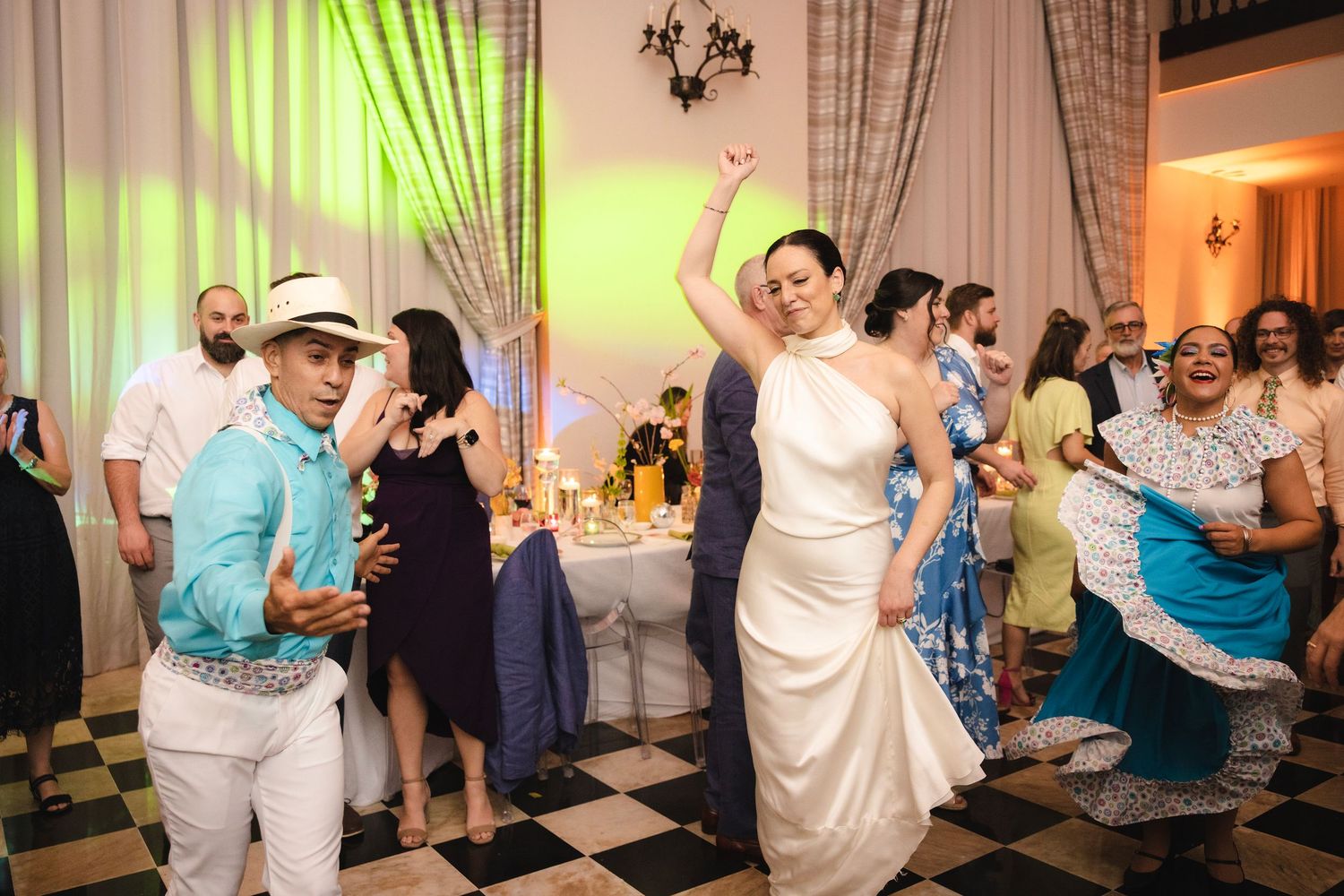 Wedding party guests dancing together in a fun conga line on the black and white checkered dance floor.