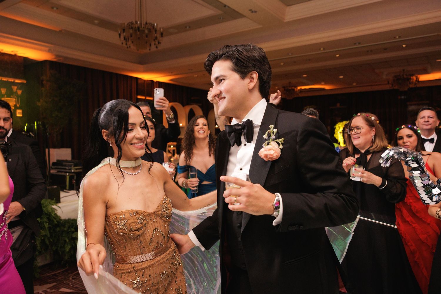 Wedding party celebrates with dancing and festivities in an elegantly decorated ballroom with warm lighting.