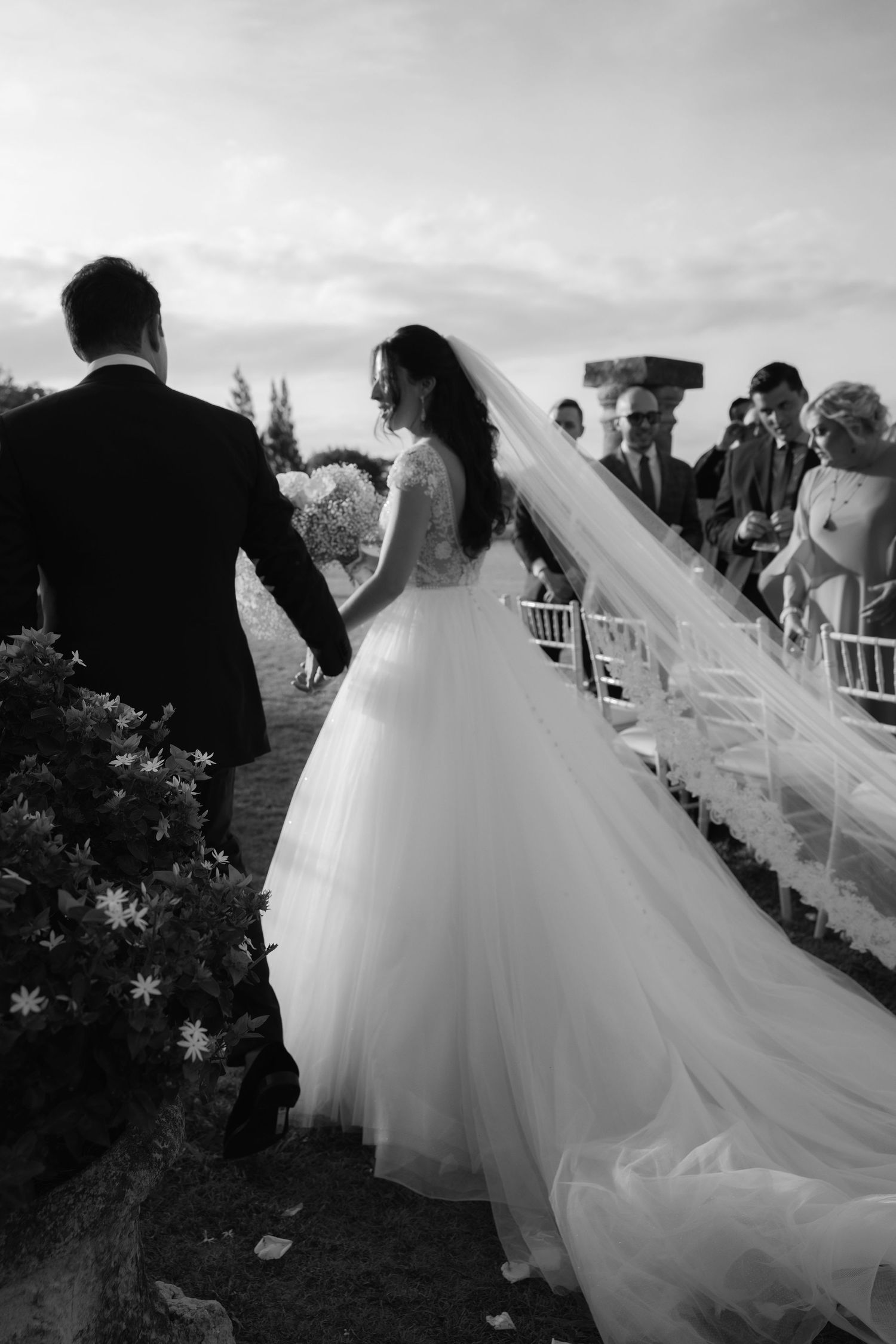 A dreamy black and white wedding photo showing a couple with a flowing veil in the breeze.