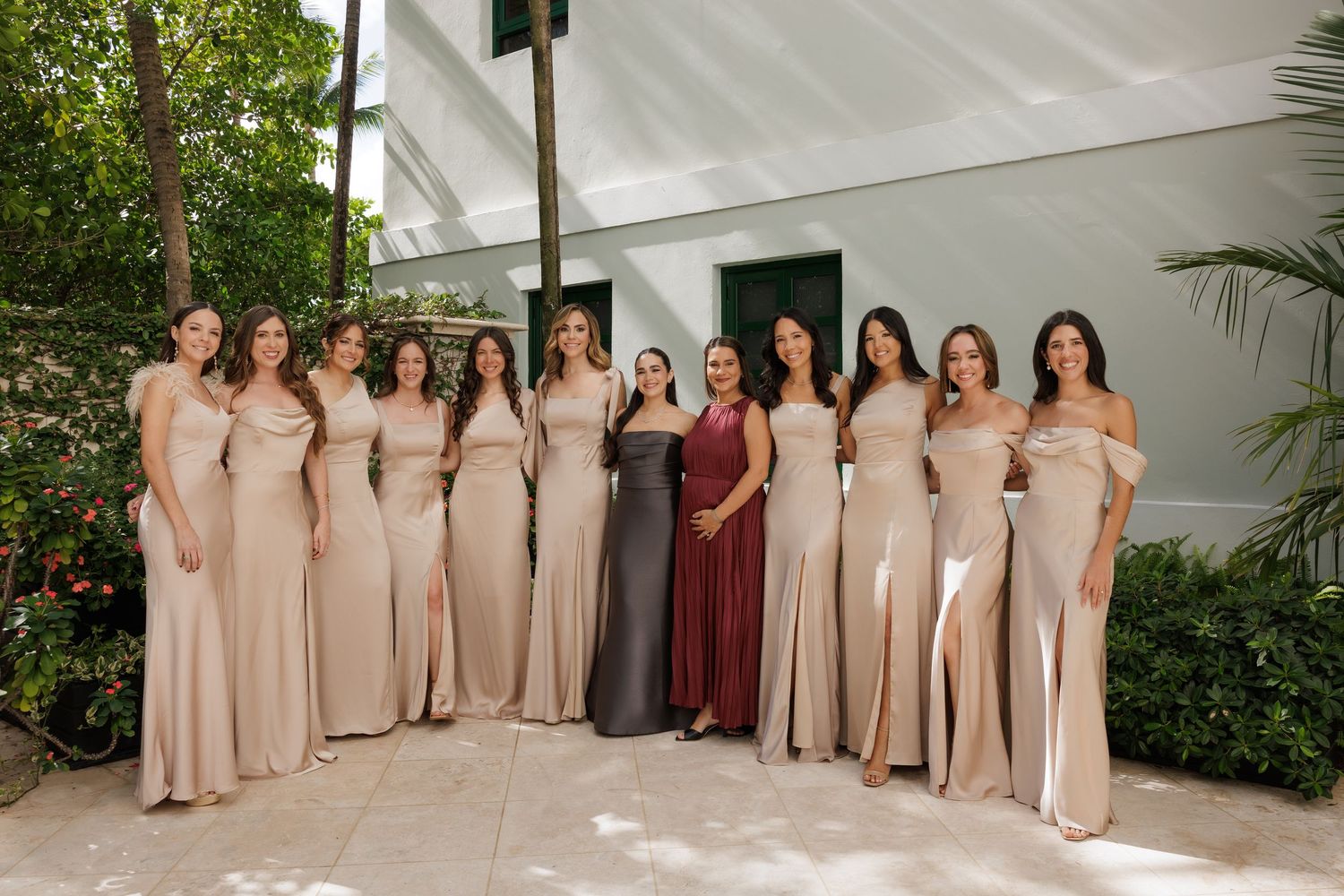 A group wearing coordinated formal dresses in neutral tones poses together in an elegant indoor setting.