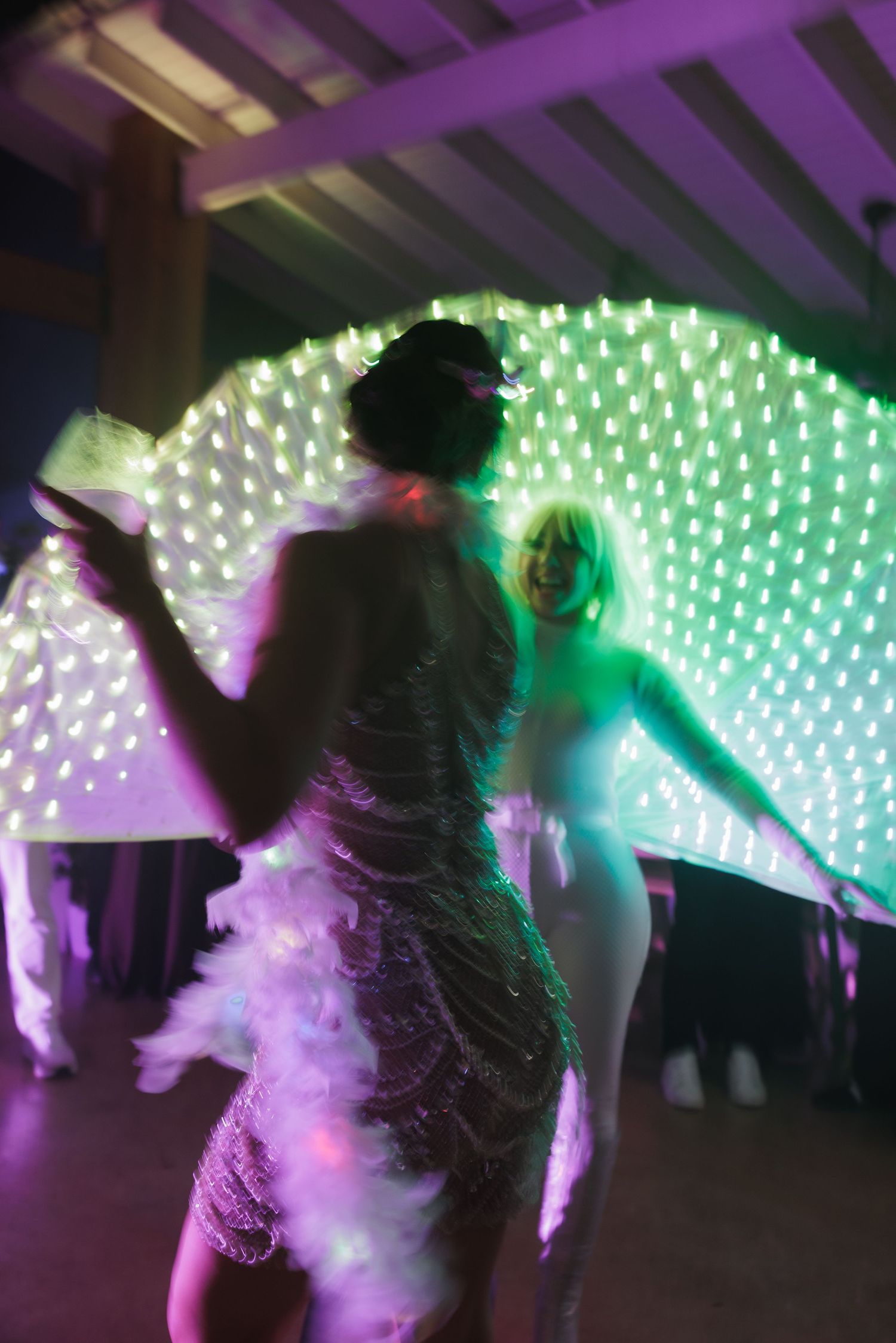 Silhouettes dancing against a backdrop of purple and green LED lights creating a dreamy atmosphere.