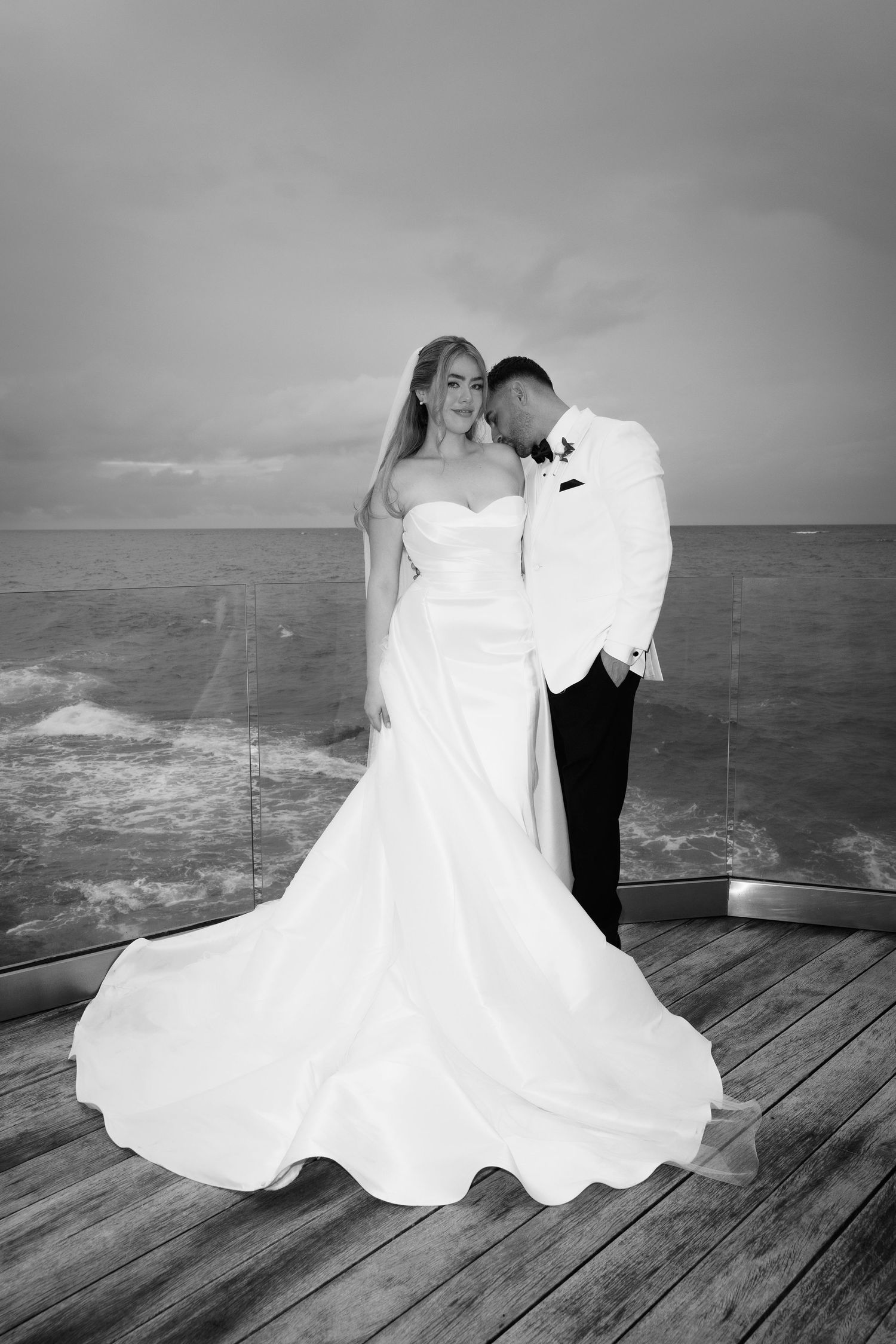 A series of black and white wedding photos showing a couple dancing on a wooden deck overlooking the ocean.
