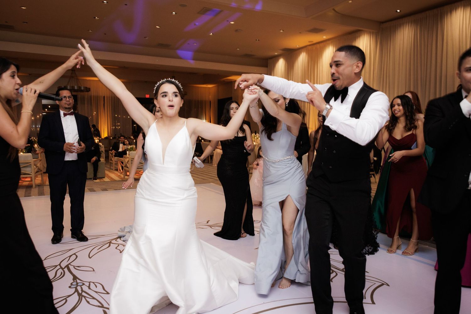 Wedding guests line up on the dance floor during a reception celebration with purple lighting and formal attire.