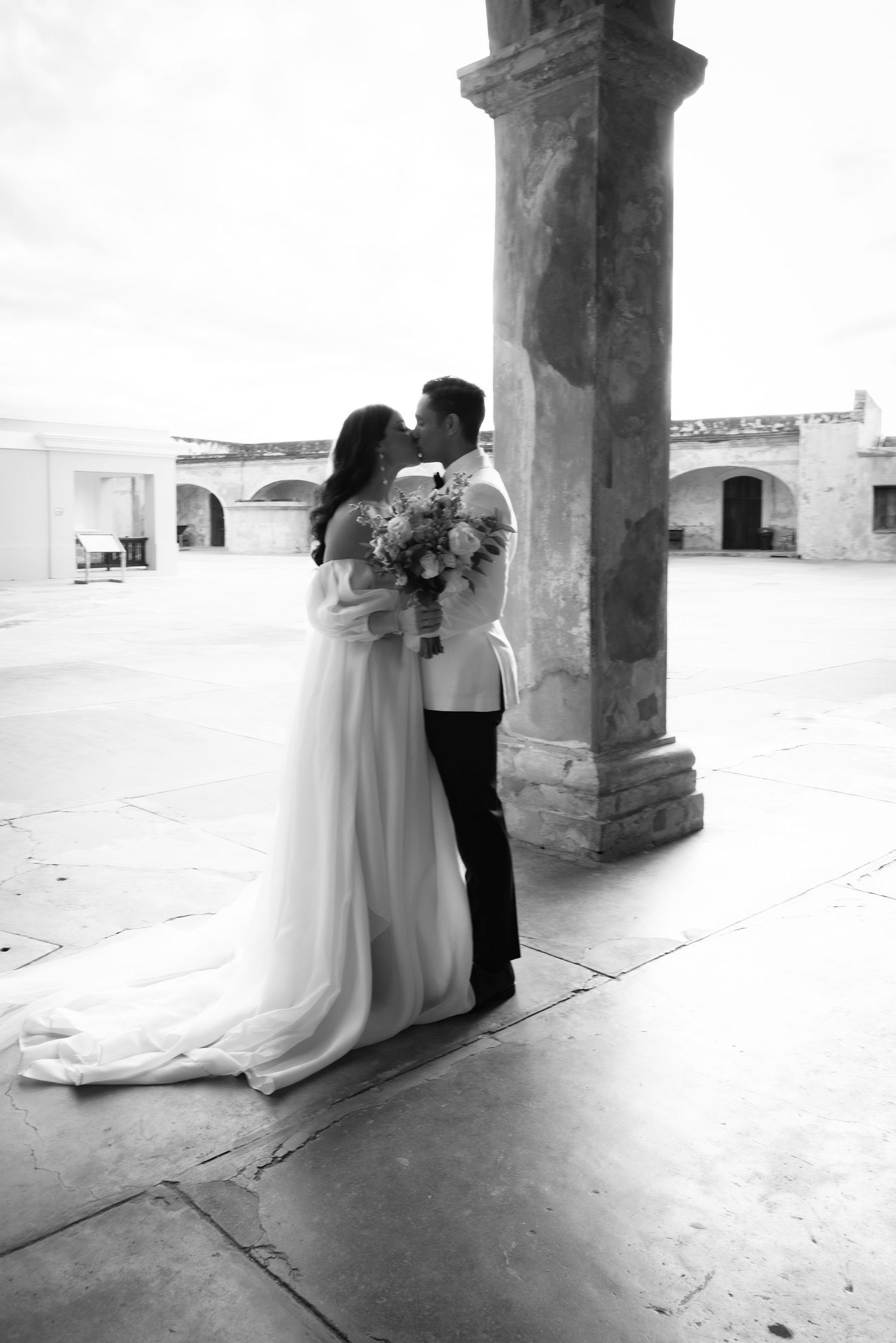 A romantic moment captured between newlyweds under stone archways in black and white.